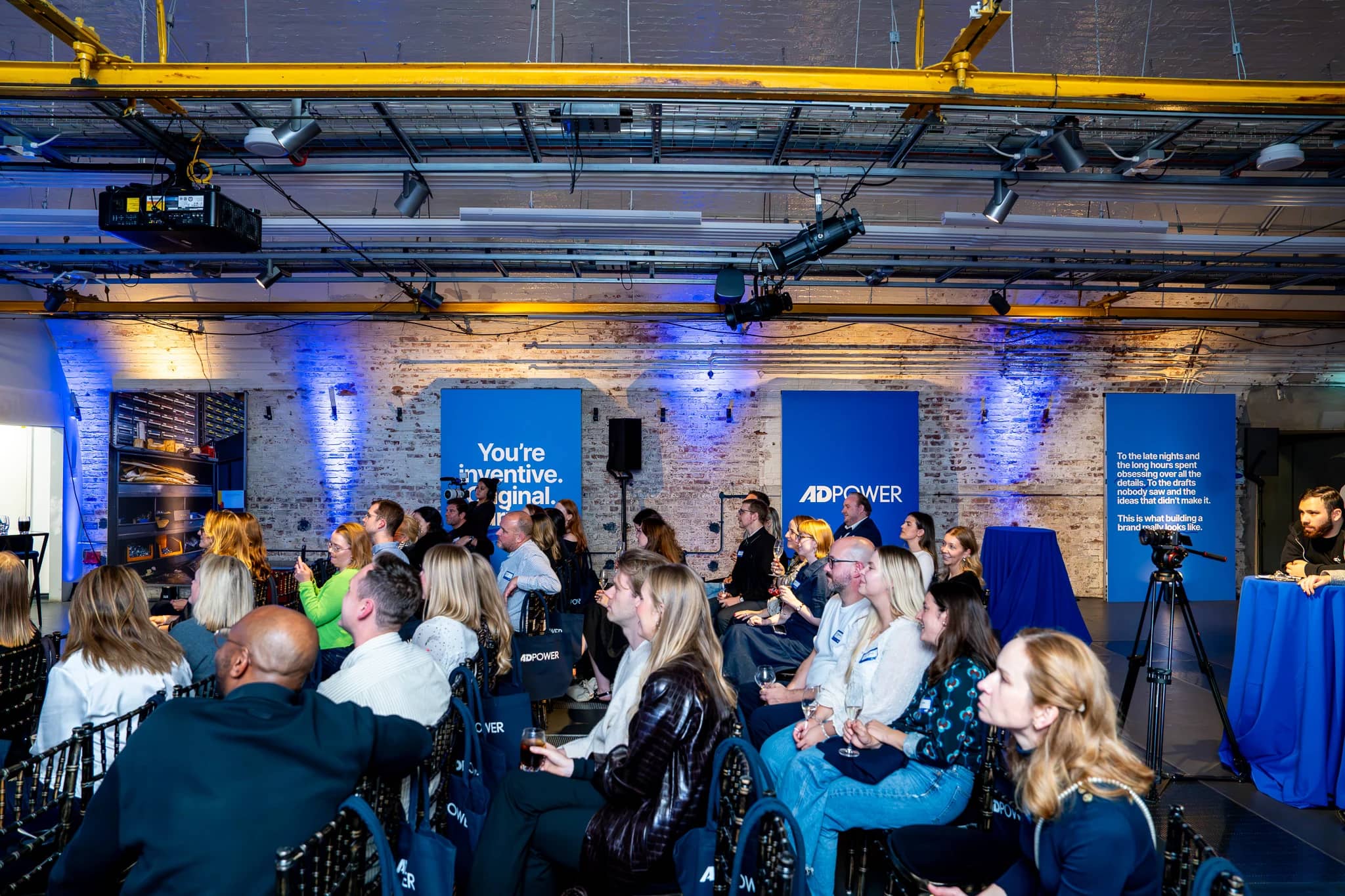 Guests watching the AdPower programme beneath the Mail Rail brick arches, with blue uplighting and printed panels along the wall.