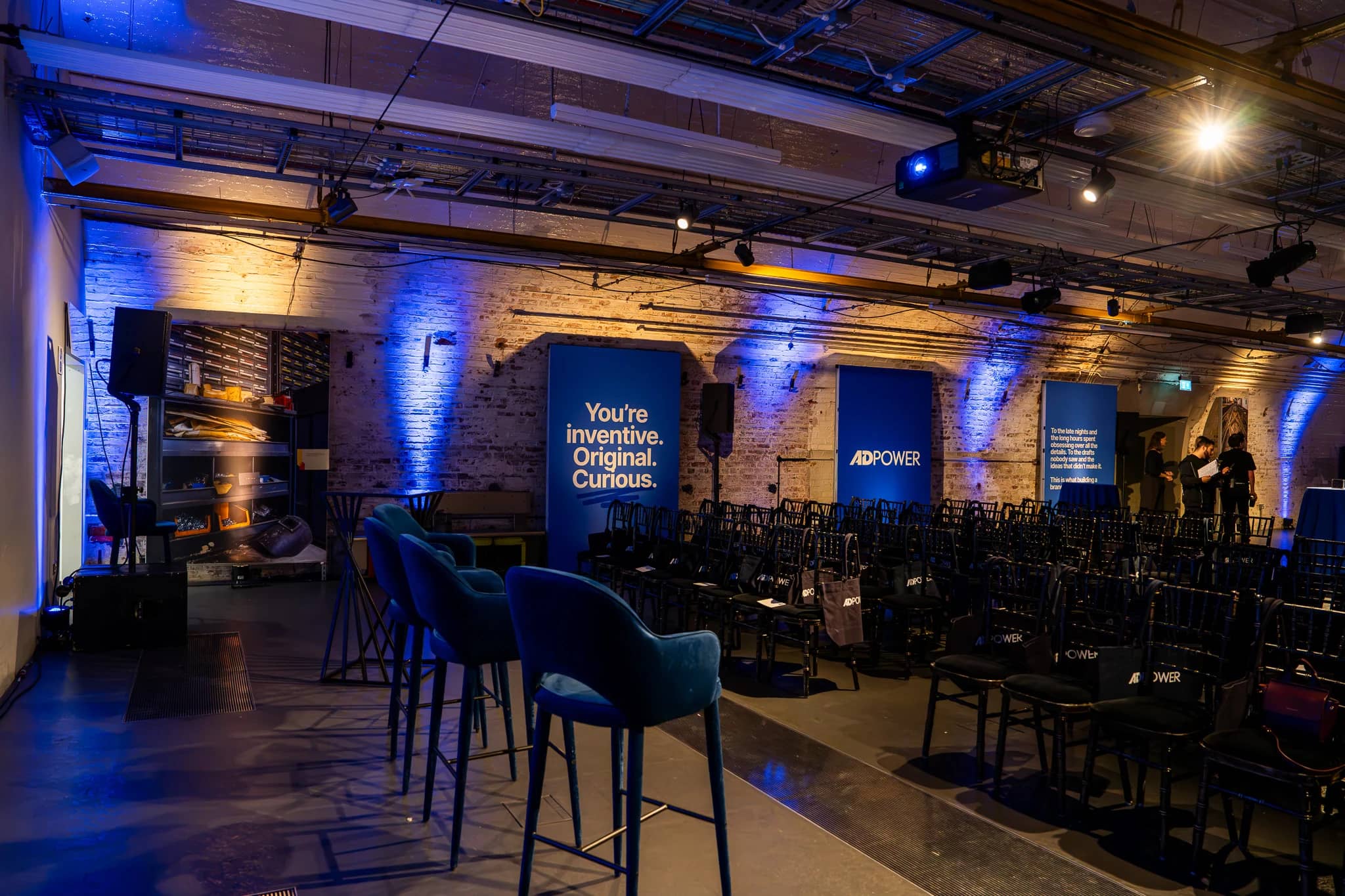Blue uplighting and tall printed AdPower panels around the Mail Rail Depot, with seating and cocktail tables ready for the evening.