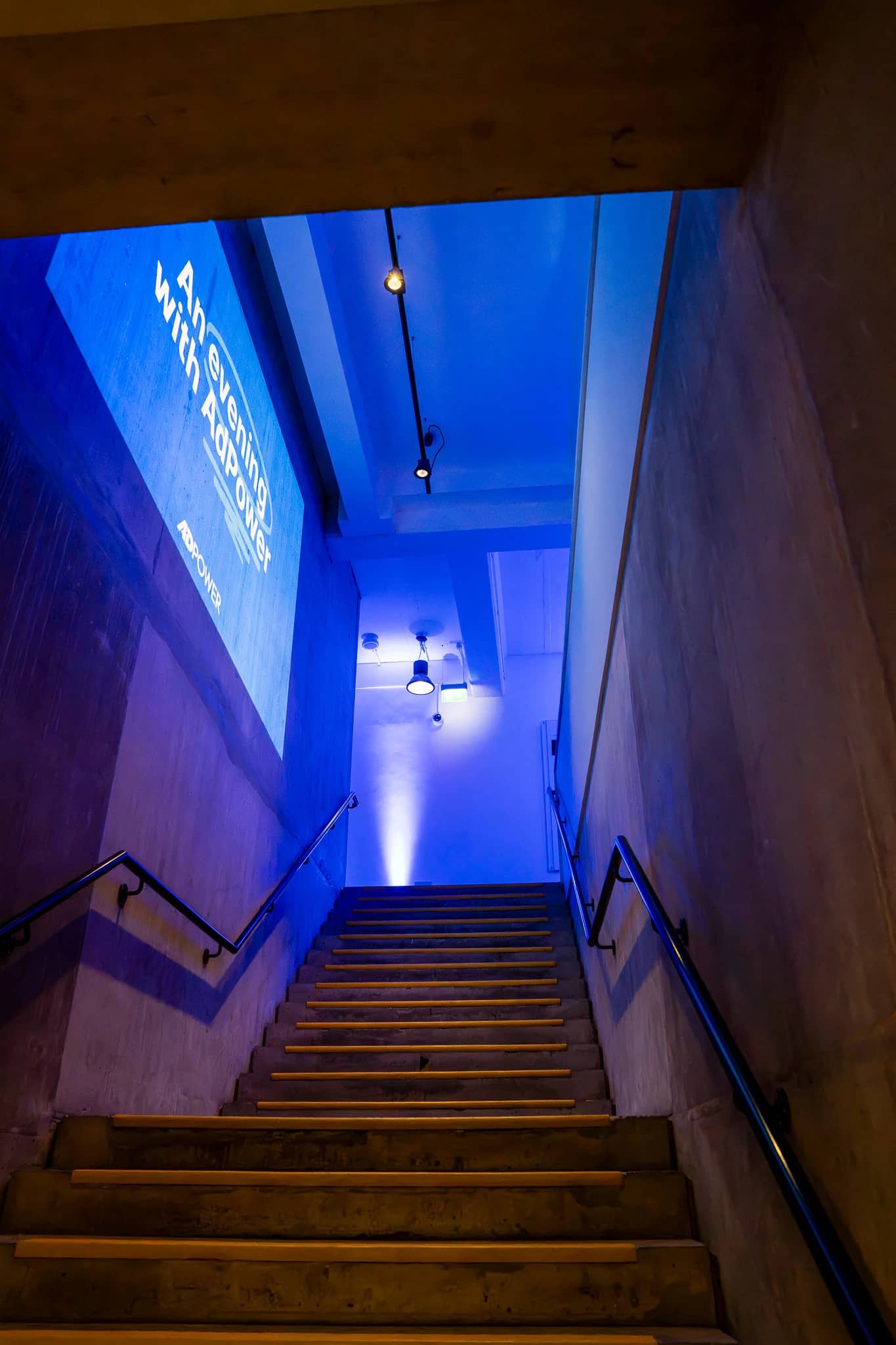 A portrait view up the staircase towards blue lighting and the projected AdPower event title at The Postal Museum.