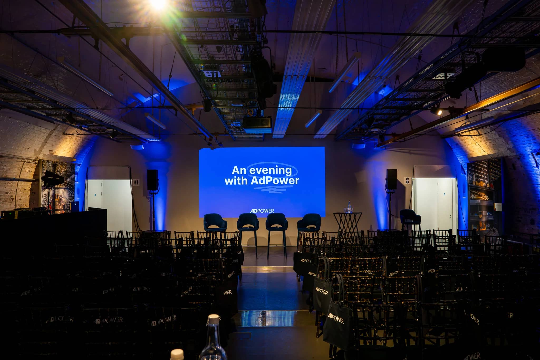 The Mail Rail Depot set for AdPower, with a projected event title, panel chairs, audience seating and blue lighting across the brick arches.