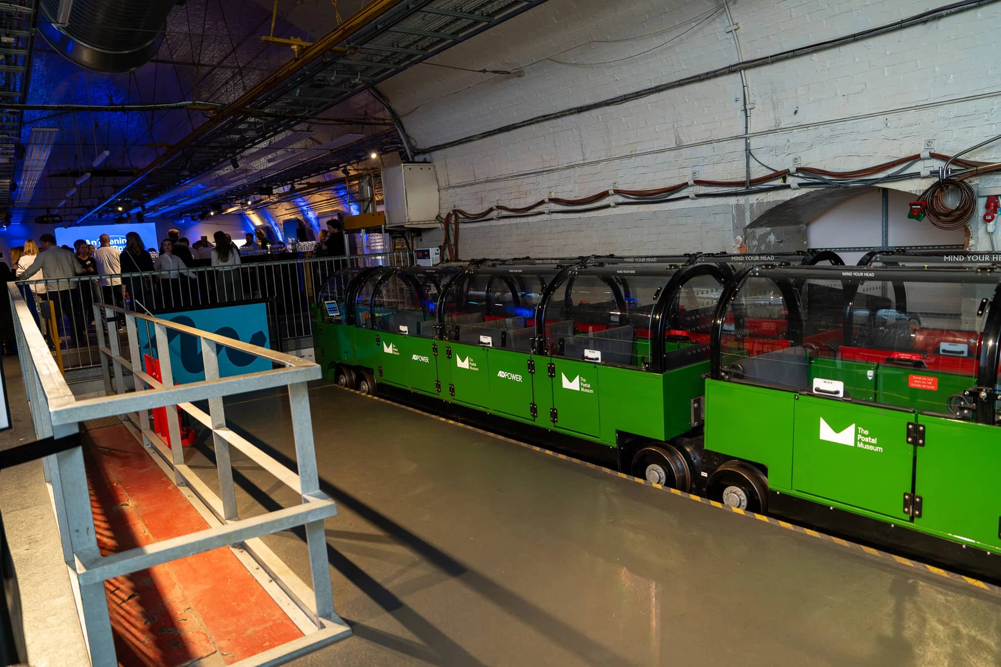 The Mail Rail train platform beside the AdPower event, with the blue-lit event space visible beyond.