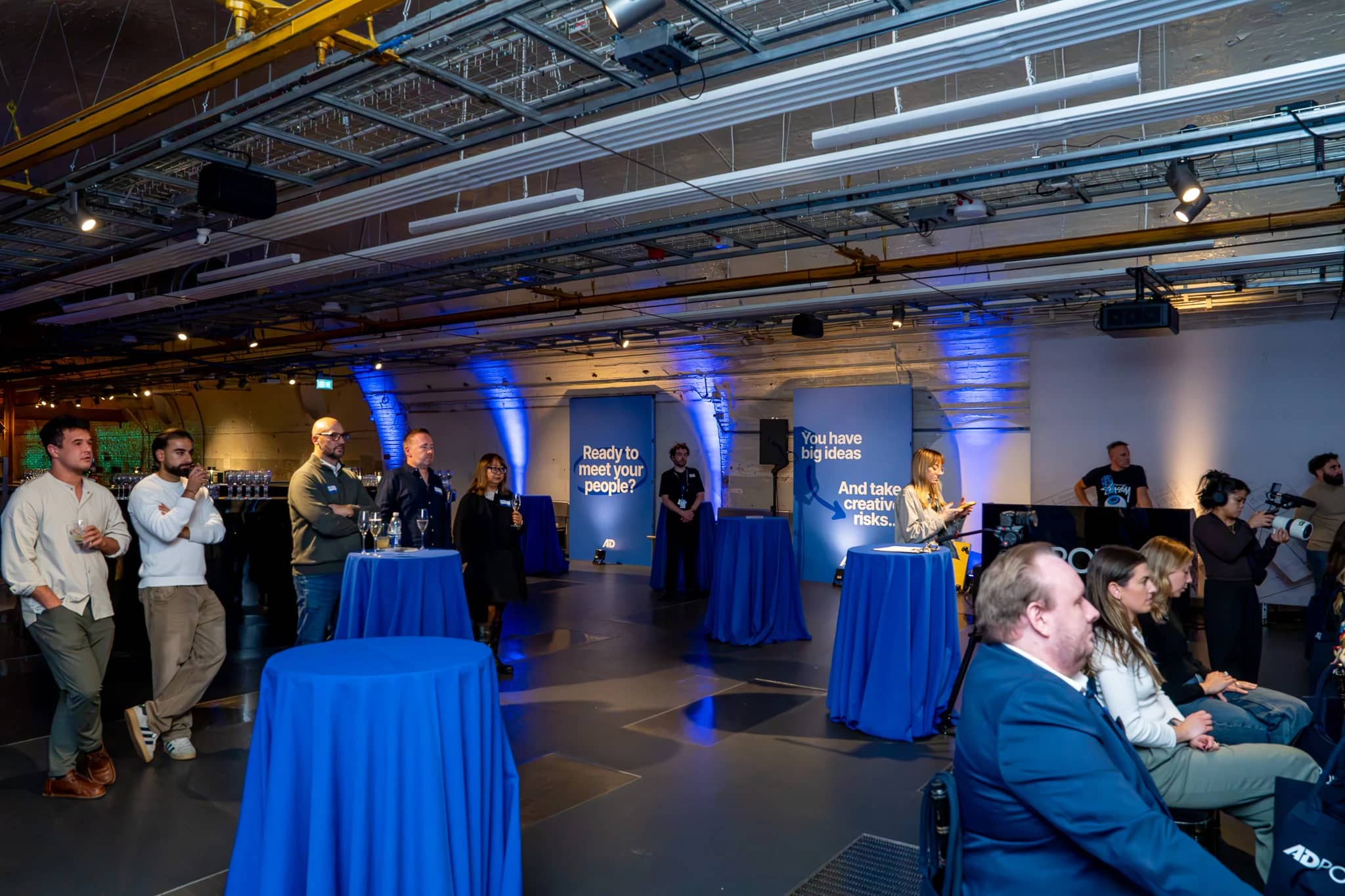 Guests and blue-covered cocktail tables beside the seated audience, with printed AdPower panels along the Mail Rail wall.