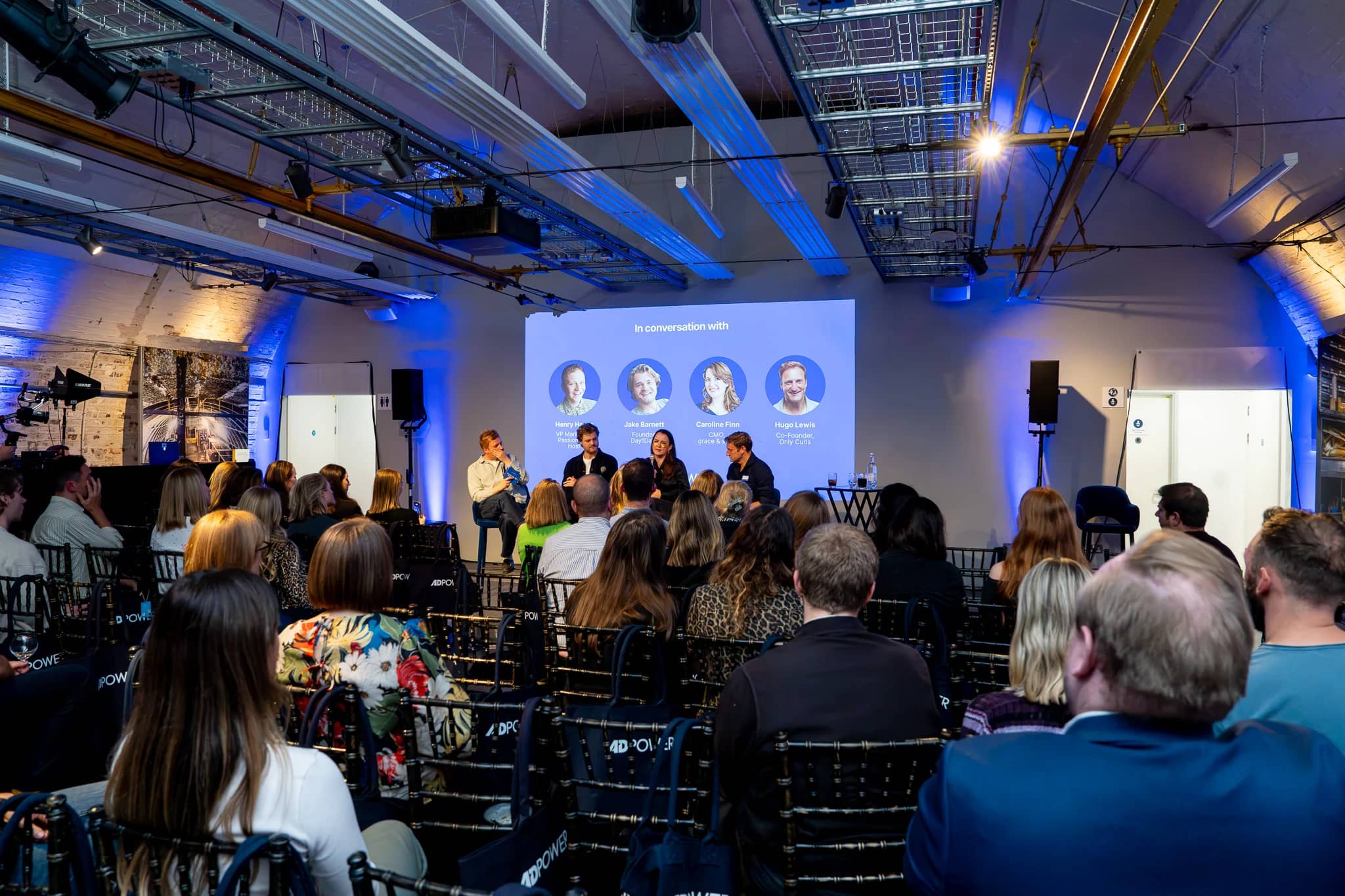 A wide view of the AdPower panel discussion and seated audience, with the panel introduction projected behind the speakers.