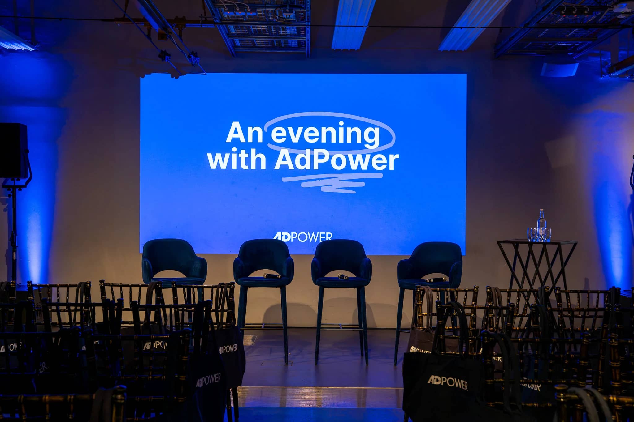 The event title An evening with AdPower projected above four panel chairs, with blue uplighting and audience seating at Mail Rail.