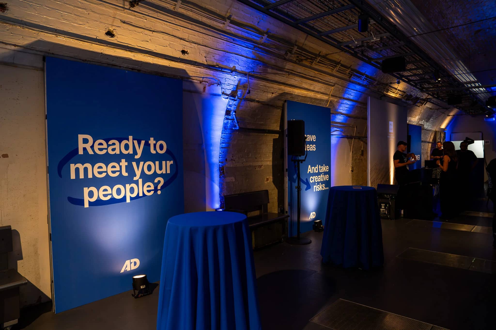 A large blue AdPower branding panel reading Ready to meet your people beside the uplighted brickwork at Mail Rail.