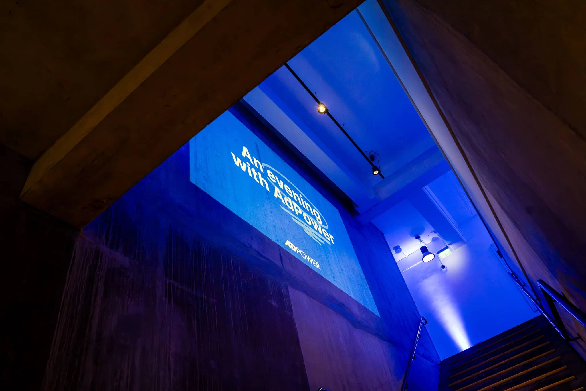 The AdPower event title projected onto the wall above the staircase, surrounded by blue lighting at The Postal Museum.
