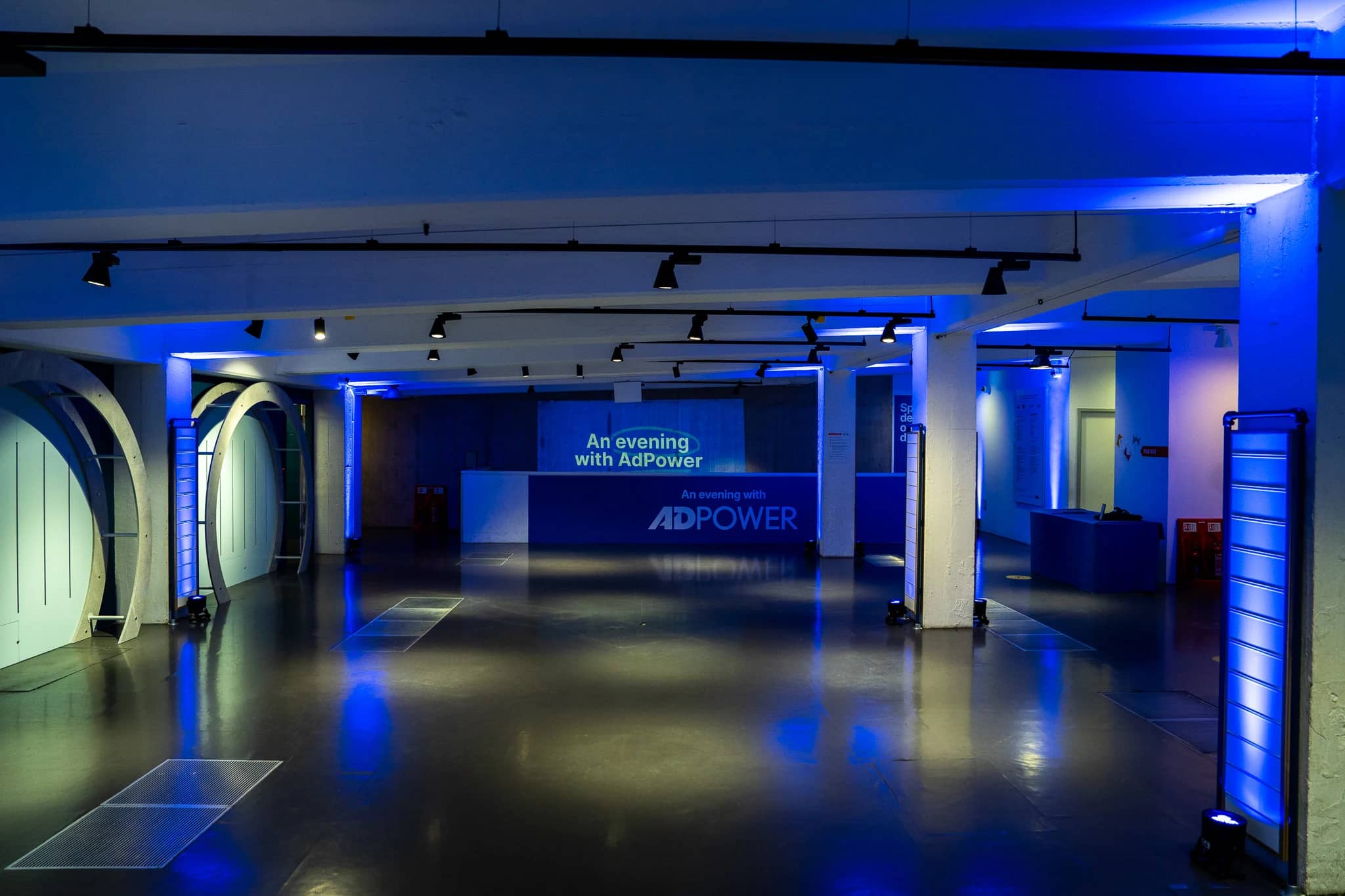 The AdPower welcome space at The Postal Museum with blue-lit columns, a branded low wall and event projection.
