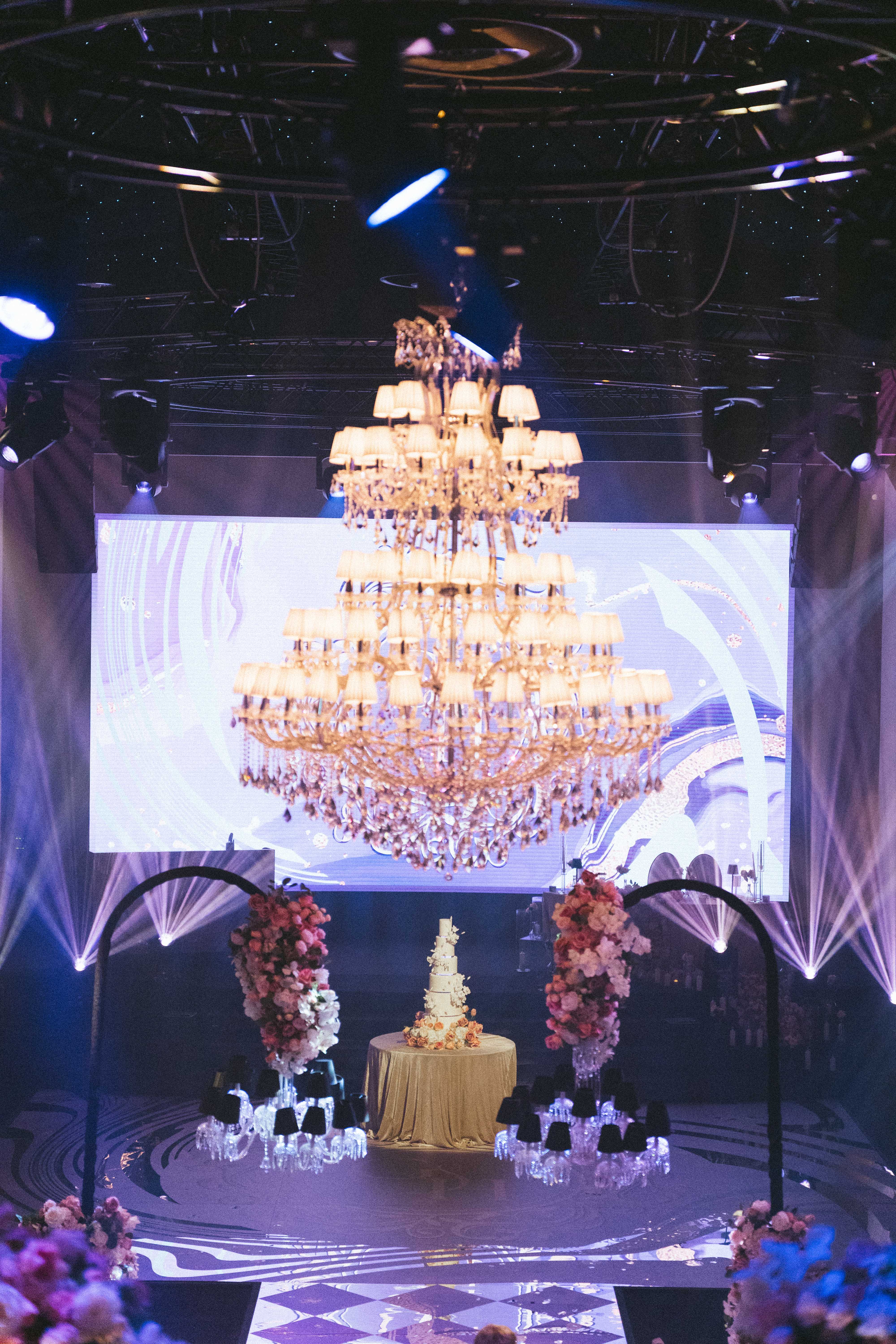 The grand chandelier and LED screen above the wedding cake display, by Kudos AV