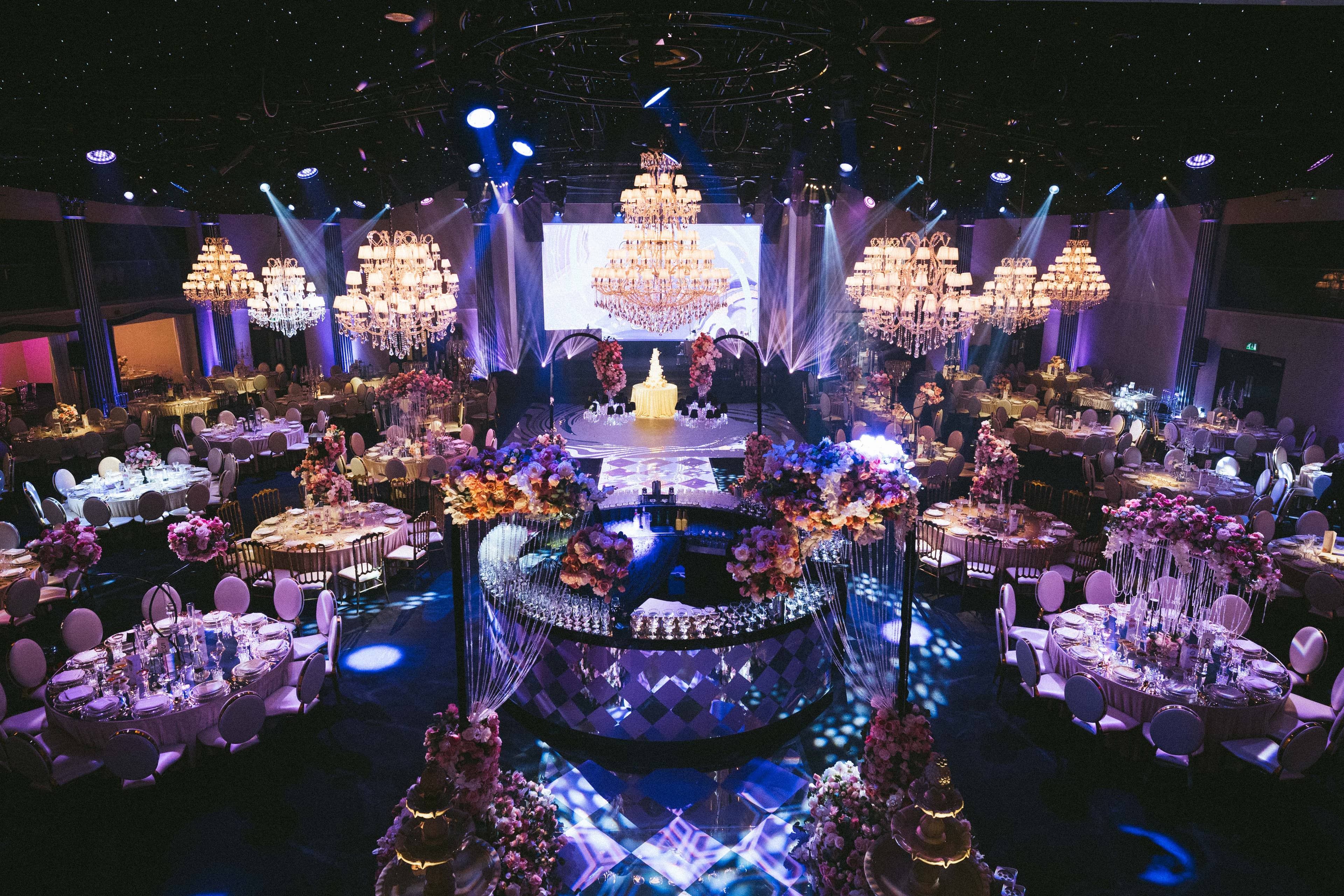 The ballroom wide with LED screen, crystal chandeliers and lilac-lit tables, by Kudos AV