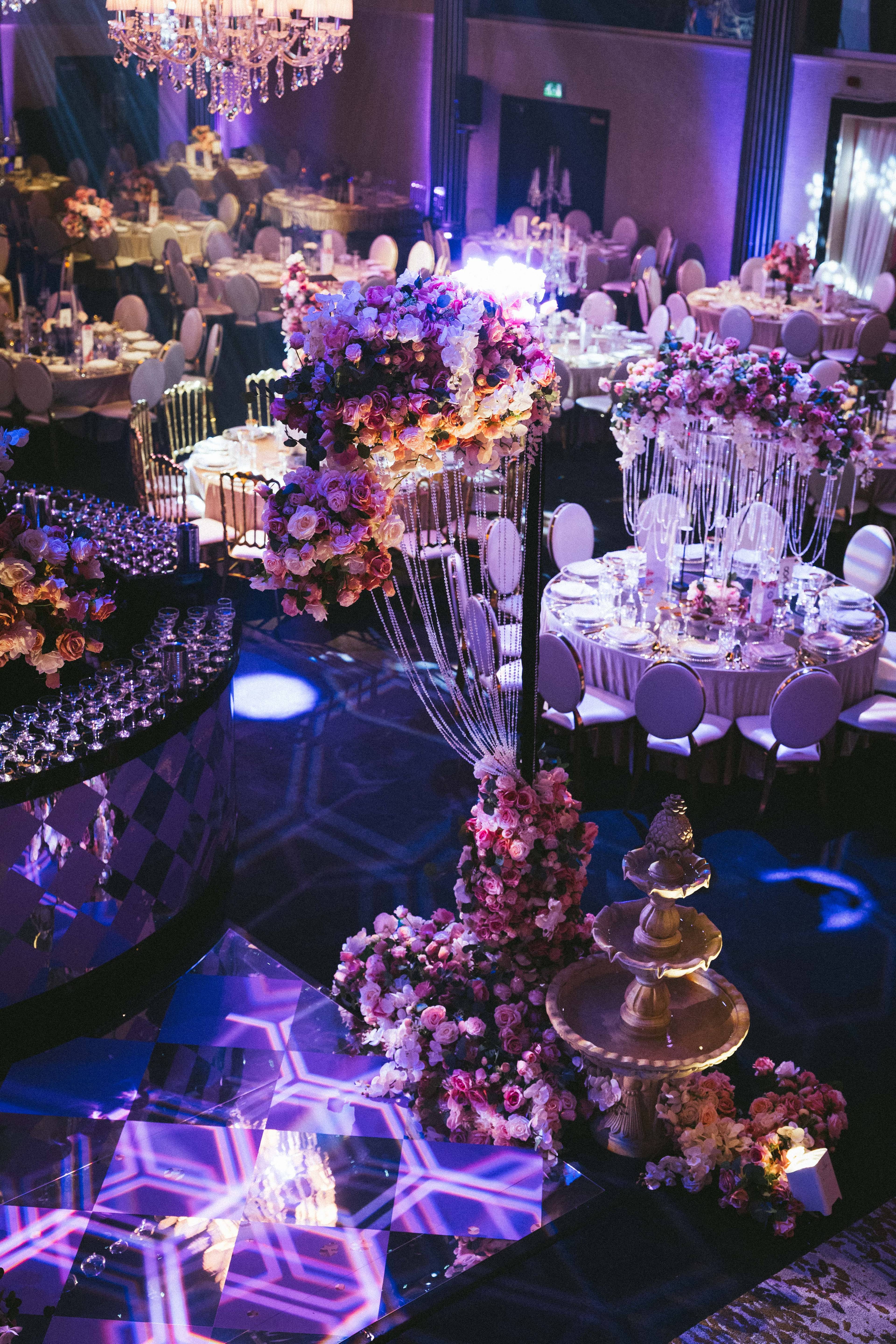 Floral centrepieces and the gold tiered cake among the tables, by Kudos AV