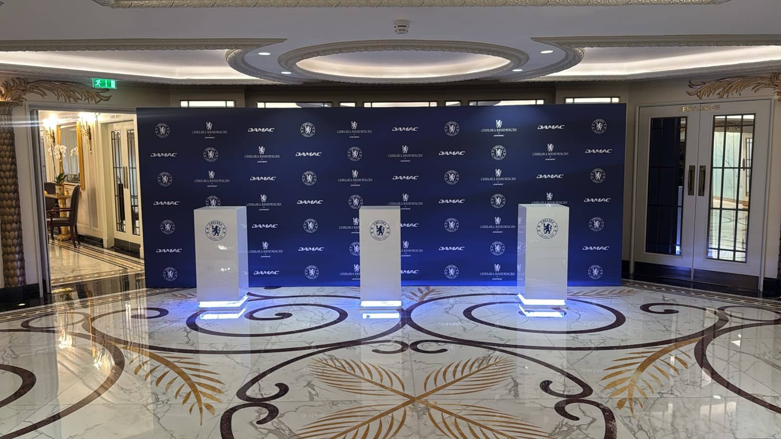 Printed Chelsea Residences media wall with three illuminated branded display plinths in a luxury hotel foyer by Kudos AV