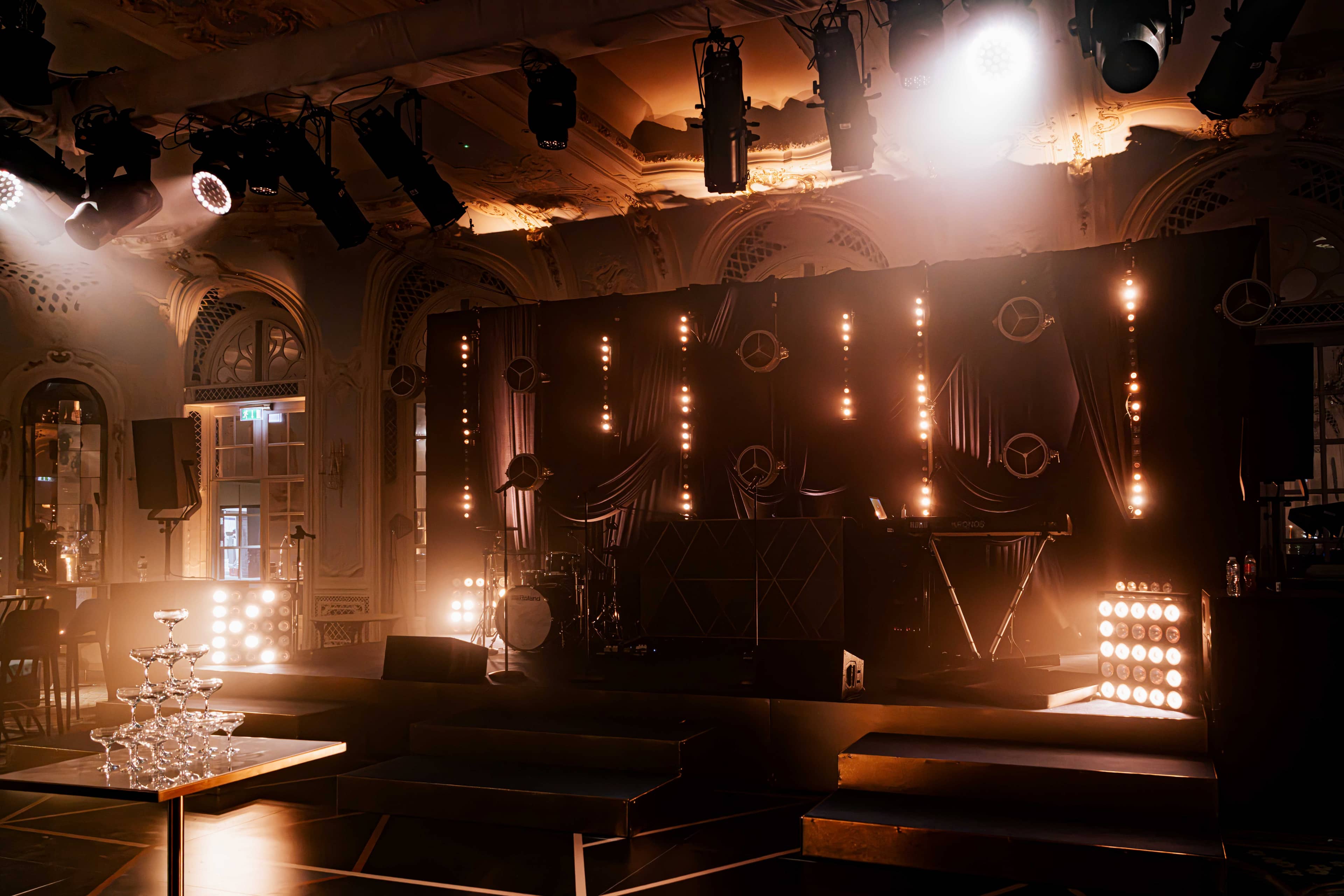 Festoon bulbs and retro lamps against black drape with moving heads on the truss, by Kudos AV