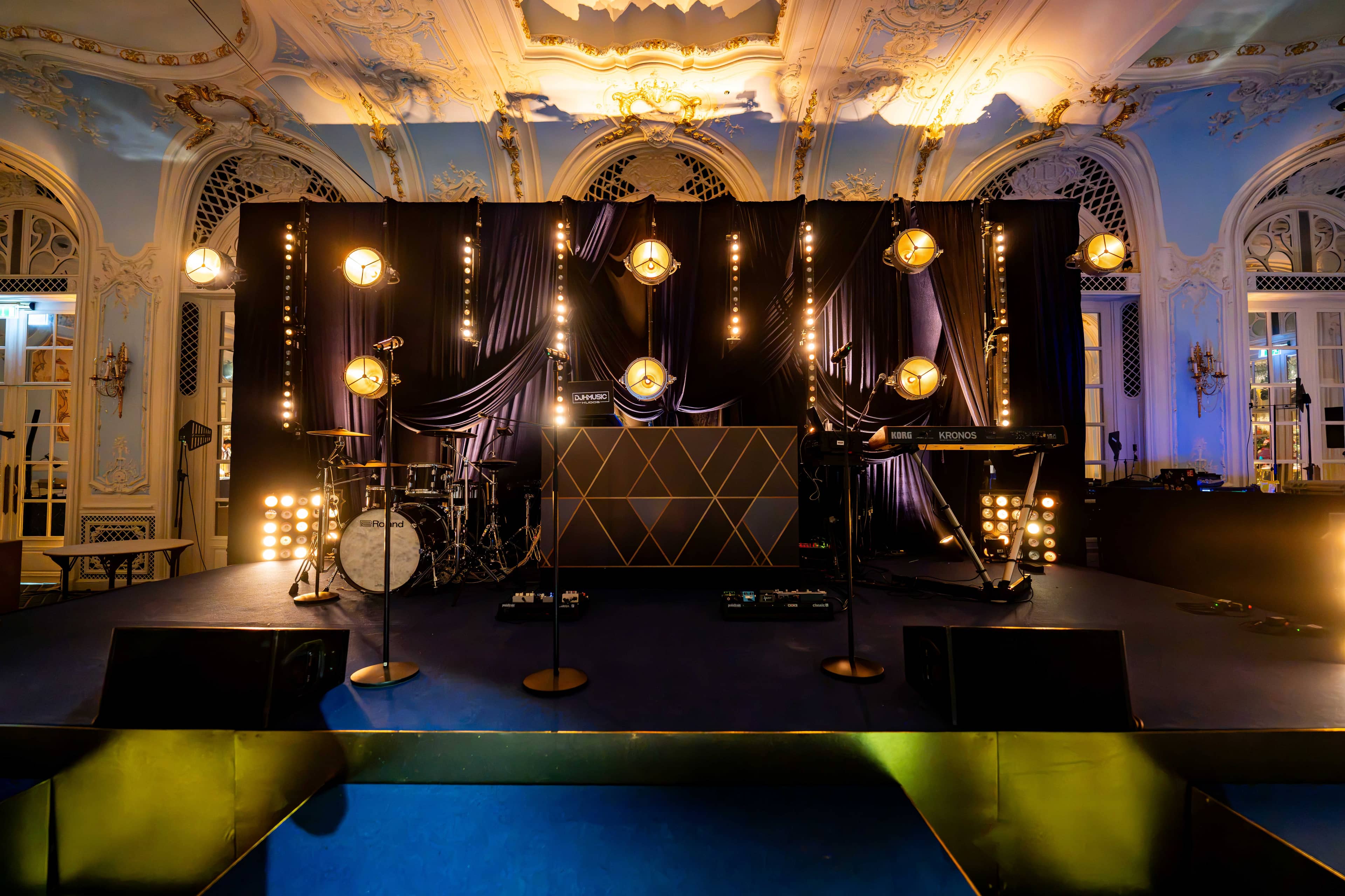 The stage wide with black drape, festoon strings and retro fixtures at The Savoy, by Kudos AV
