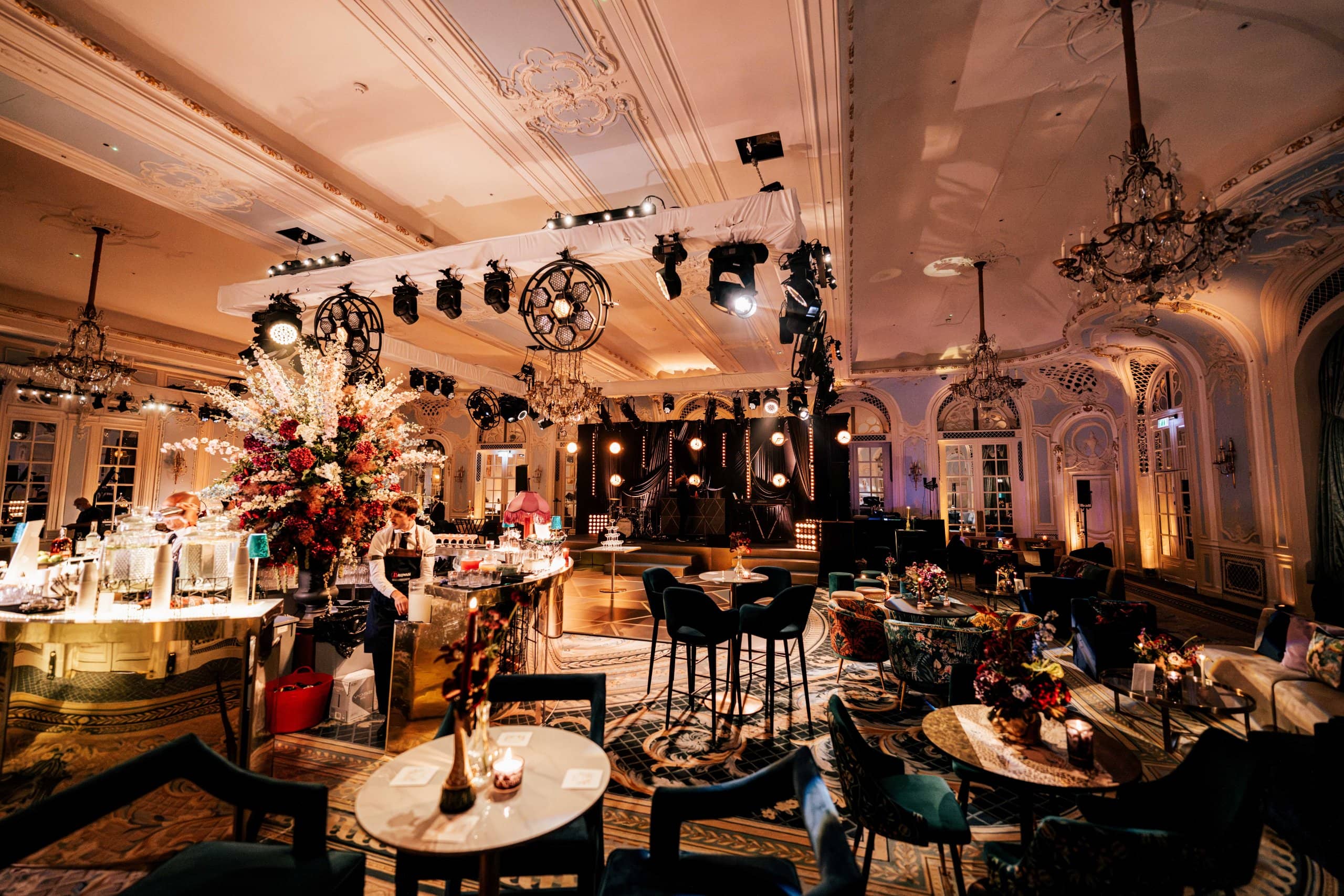 The Savoy wedding room wide from the bar corner, candlelit poseur tables and the stage beyond, by Kudos AV