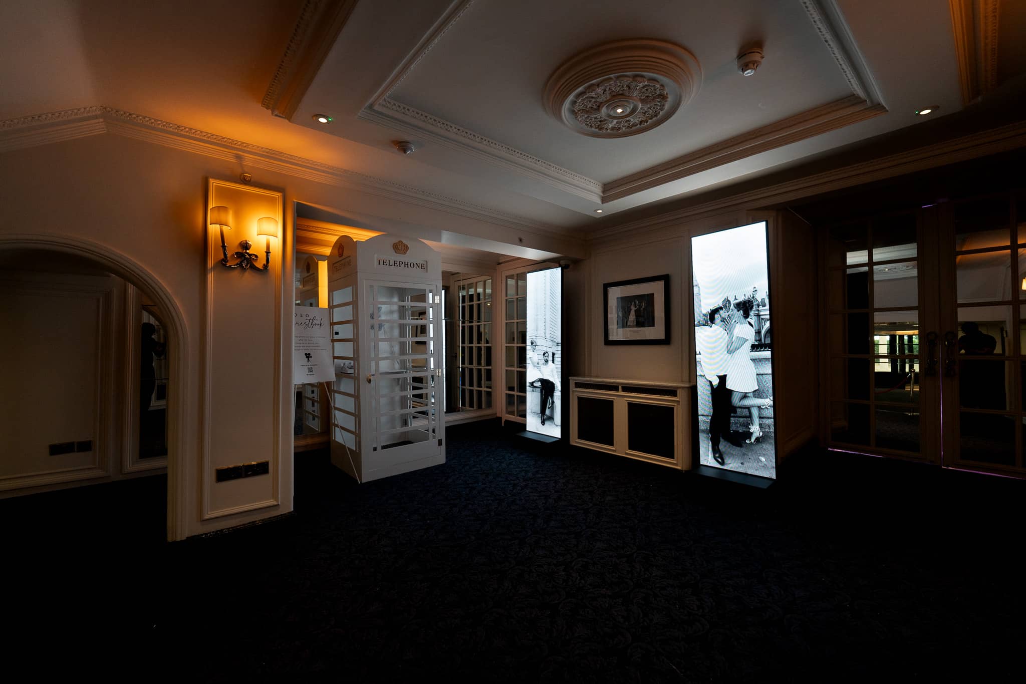LED totems glowing along the panelled corridor at The Savoy beside the hotel's white telephone box, by Kudos AV