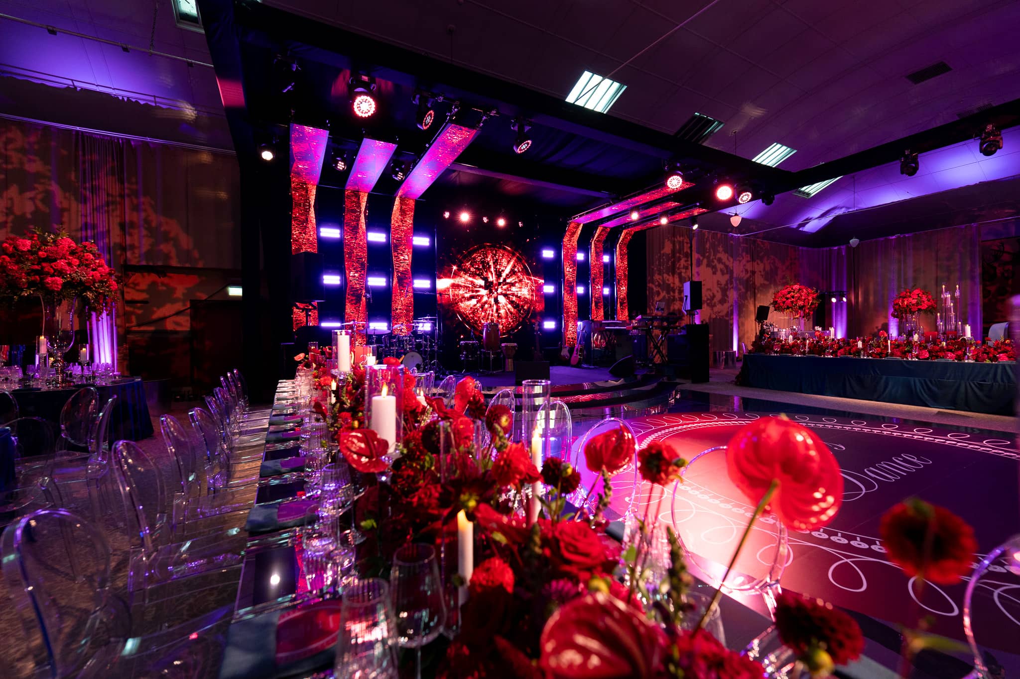 Tatton Park wedding in the Tenants' Hall, red floral centrepieces under purple uplighting, produced by Kudos AV
