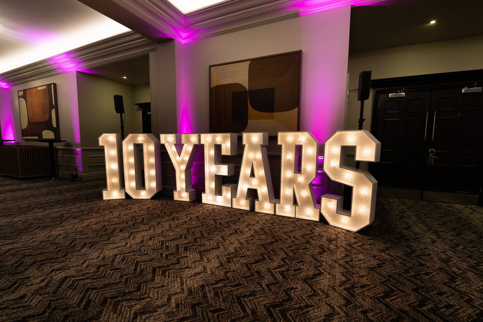 Giant 10 YEARS marquee light up letters glowing warm white under pink uplighting in the foyer at Verve Awards Night, Sopwell House.