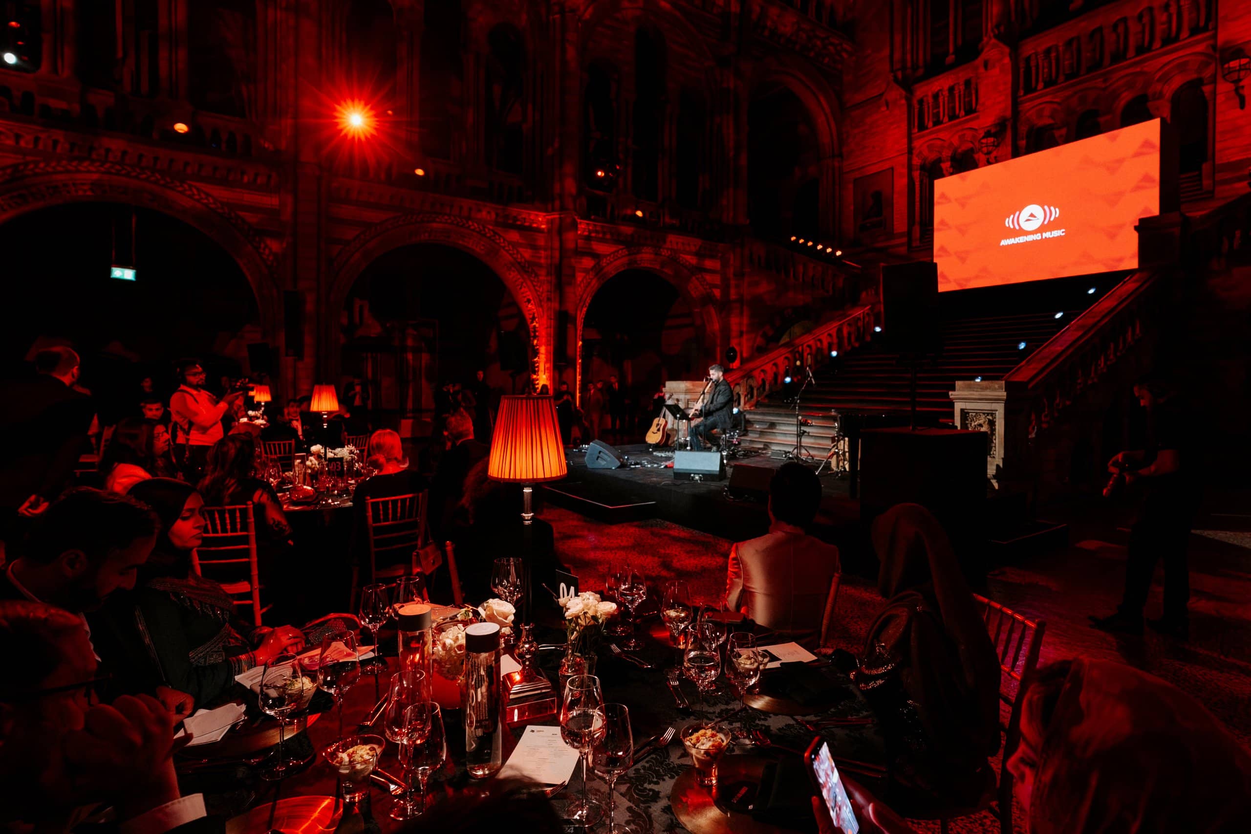 The band on stage in front of the Unilumin LED screen as guests dine in Hintze Hall, Awakening Music 25th anniversary at the Natural History Museum, by Kudos AV.