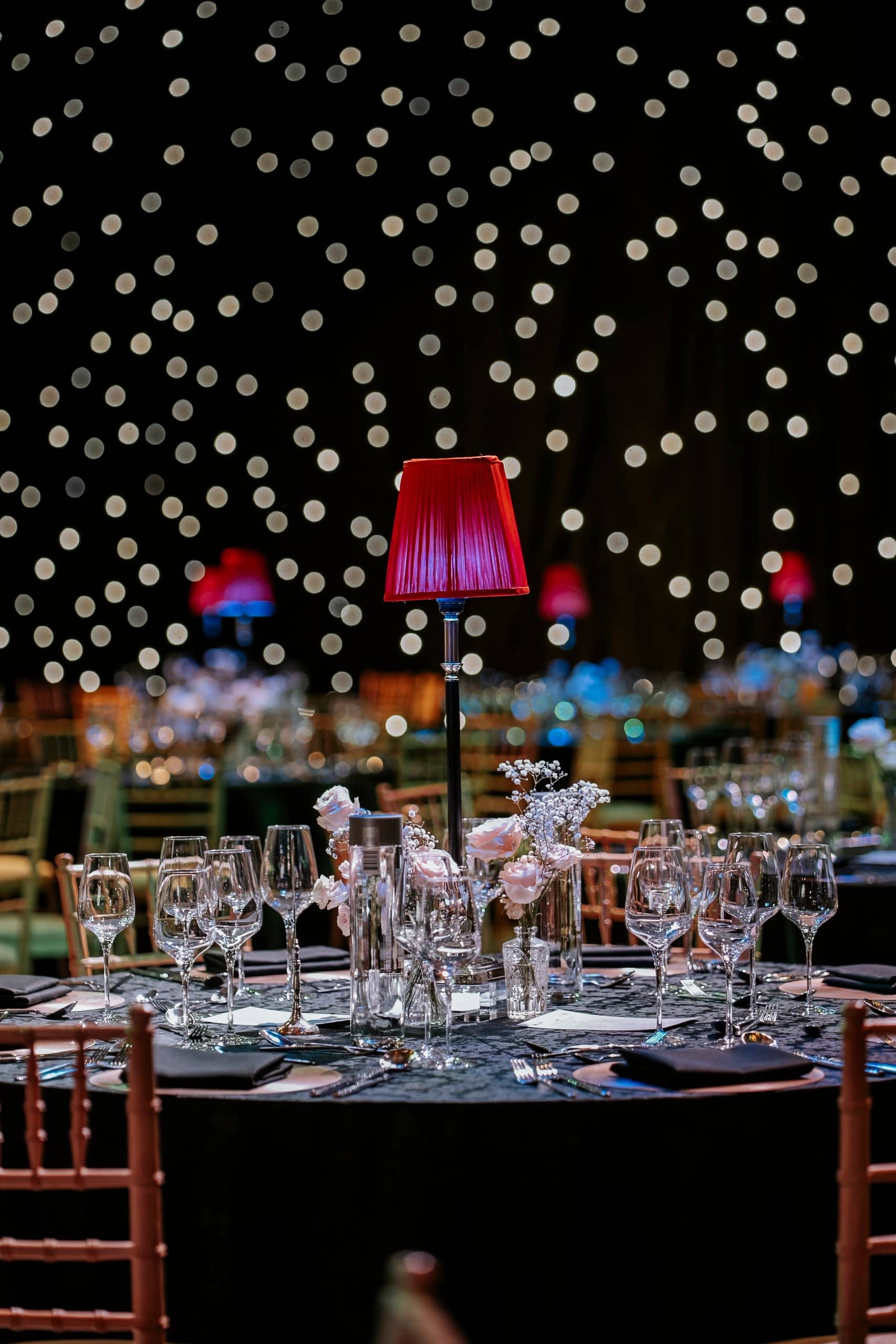 A table setting with a red lamp, glassware and white florals at the Awakening Music 25th anniversary dinner at the Natural History Museum.