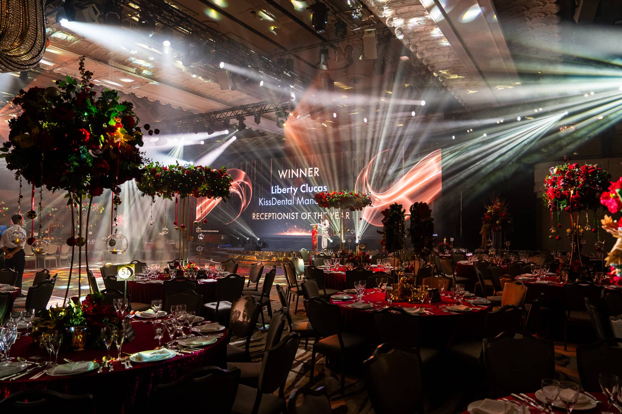A winner announcement on the LED screen during the ceremony, the stage lit and the tables dressed in red florals, Dental Beauty Partners Awards 2025 in the Great Room at Grosvenor House London, by Kudos AV.