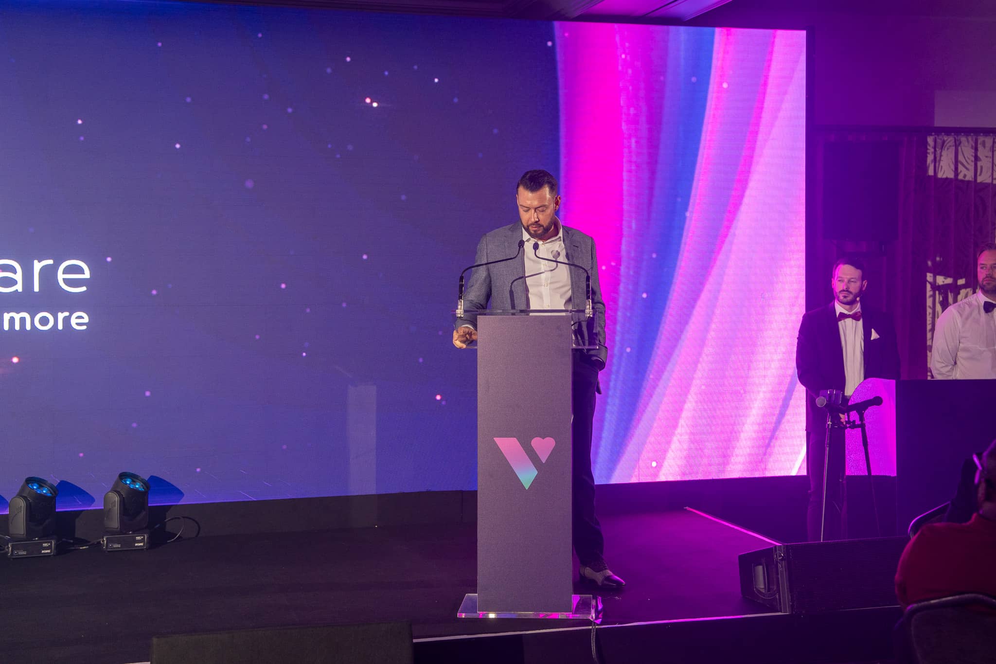 A presenter speaks from the branded acrylic lectern at Verve Awards Night, with the Verve Homecare LED wall and stage lighting behind, Sopwell House.