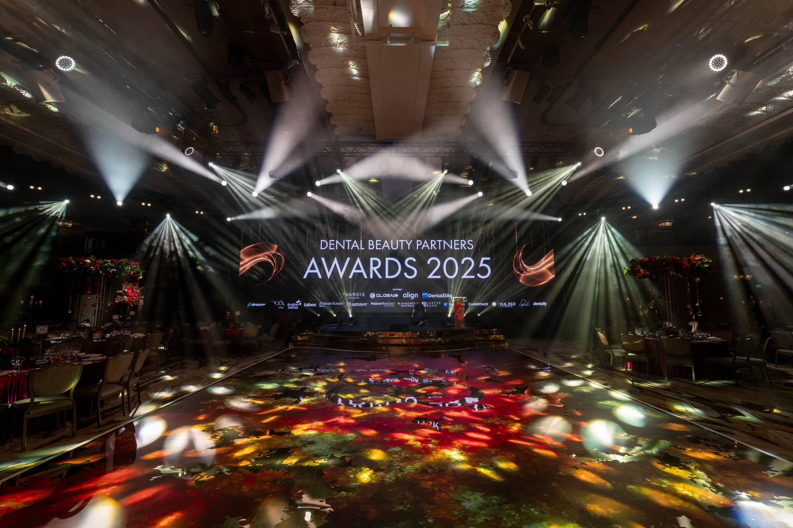 Beam lighting from the truss over the stage, the LED screen and the printed dancefloor lit up at the Dental Beauty Partners Awards 2025 in the Great Room at Grosvenor House London, by Kudos AV.