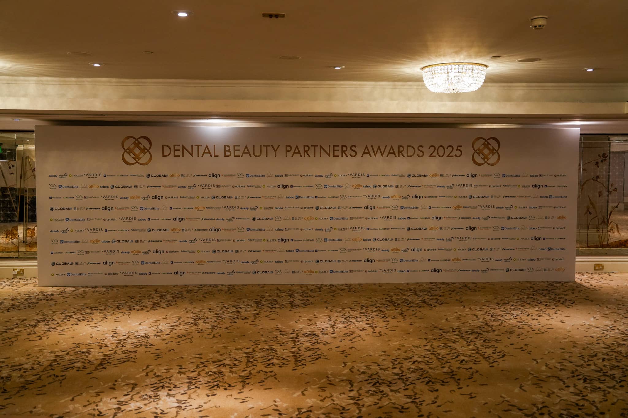 The Dental Beauty Partners Awards 2025 backdrop wall with the partner logos, lit for arrival photographs in the Great Room at Grosvenor House London, by Kudos AV.