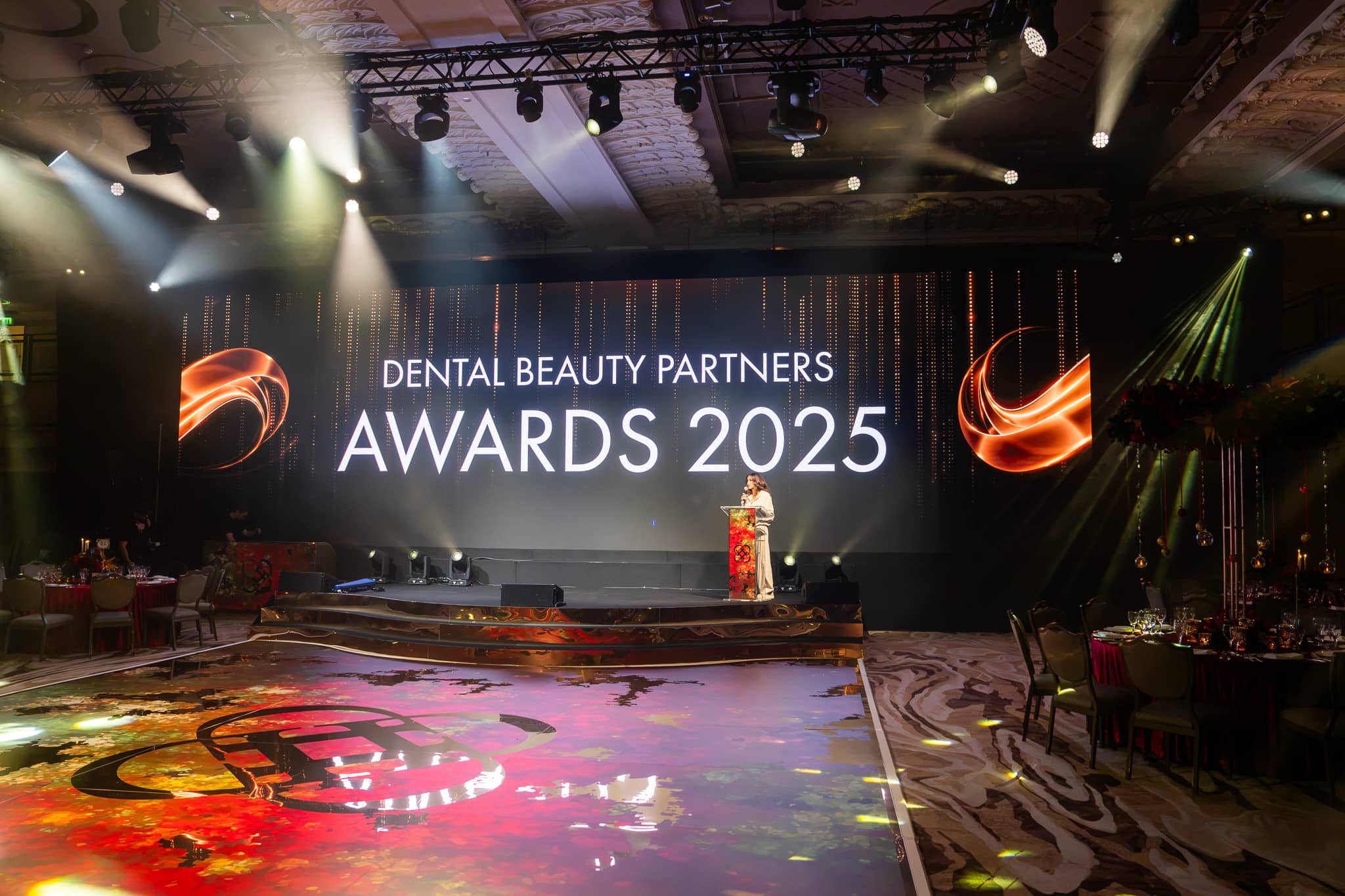 The Dental Beauty Partners Awards 2025 title on the wide LED screen above the stage, beams from the overhead truss and the printed dancefloor in front, in the Great Room at Grosvenor House London, by Kudos AV.