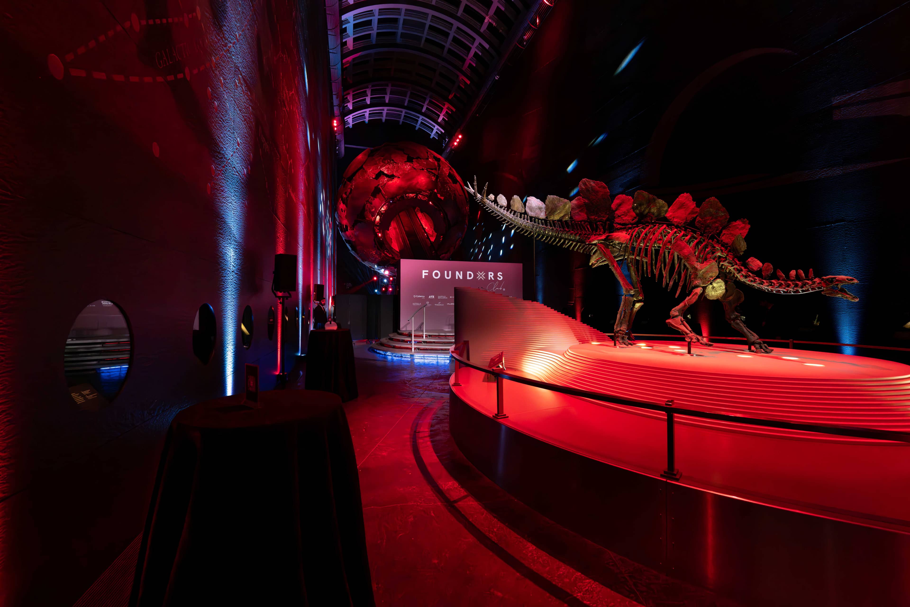 The Stegosaurus at the entrance to Earth Hall lit red with blue accents for the FOUNDXRS Club black tie party at the Natural History Museum, by Kudos AV.