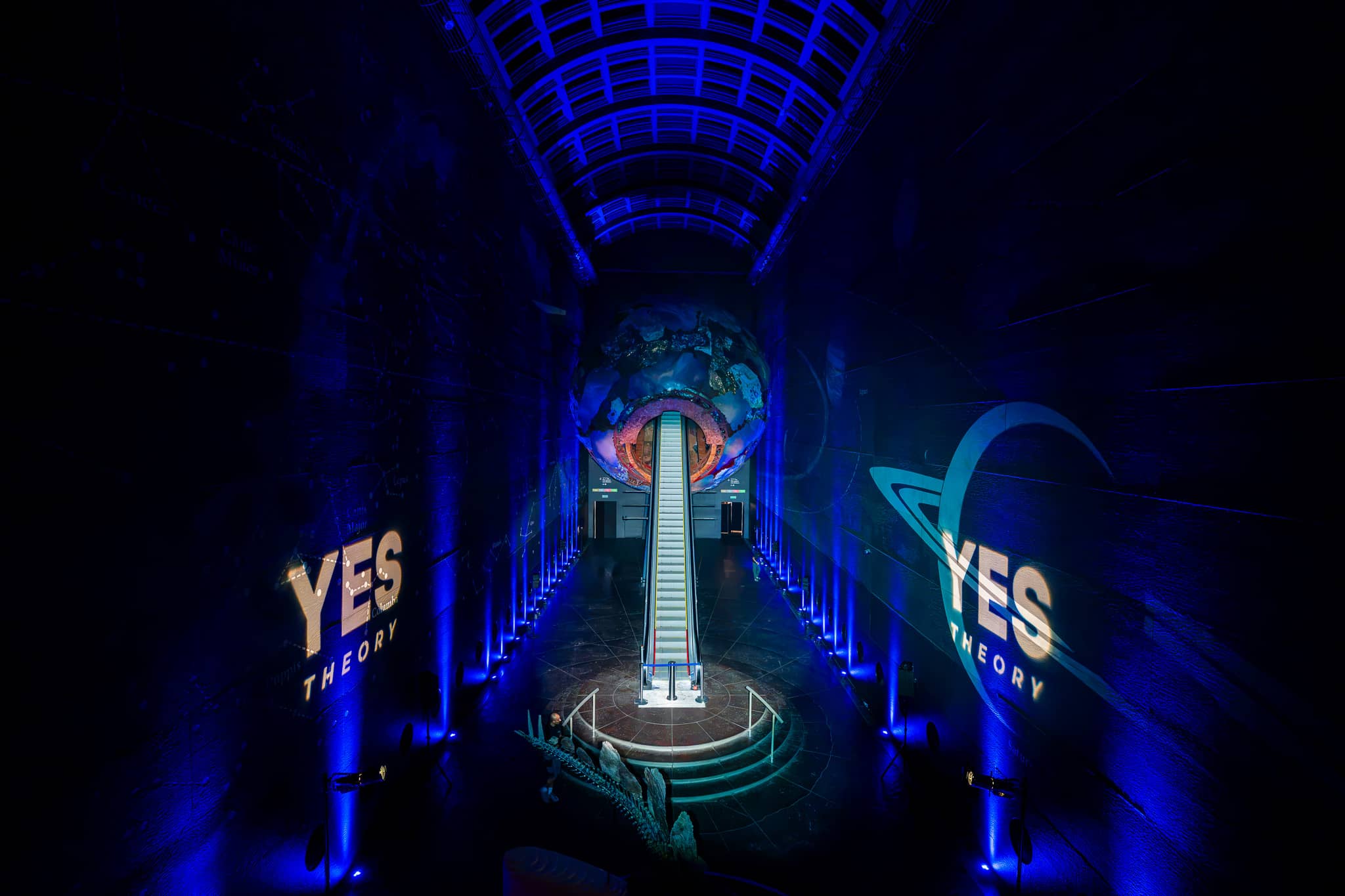 The Earth sculpture glowing at the top of the escalator in Earth Hall, the hall washed blue by Kudos AV for the Yes Theory 10 million subscriber celebration.