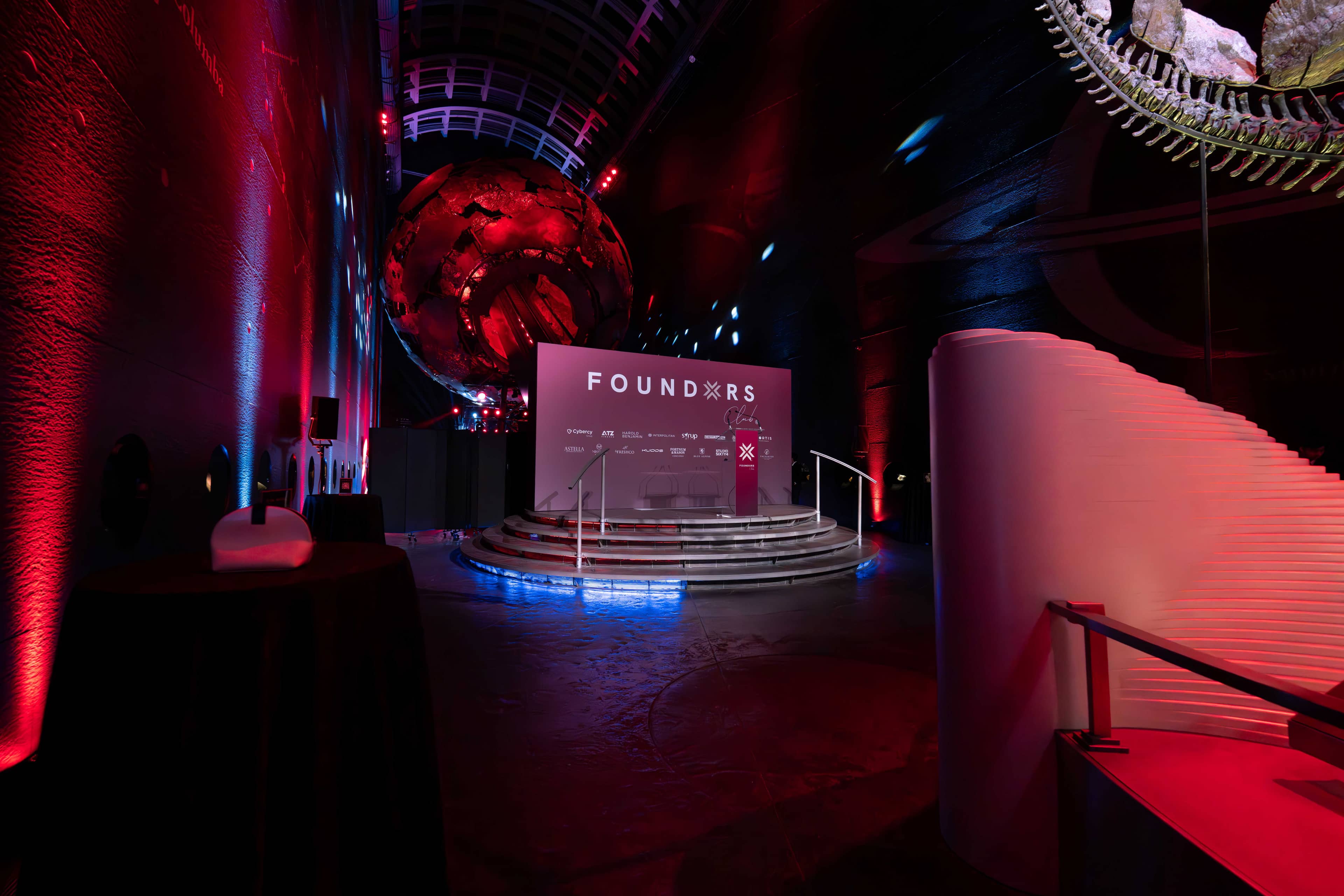 The printed FOUNDXRS stage backdrop in Earth Hall, red uplighting on the walls and blue light along the base of the curved balconies, FOUNDXRS Club black tie party printed and lit by Kudos AV.