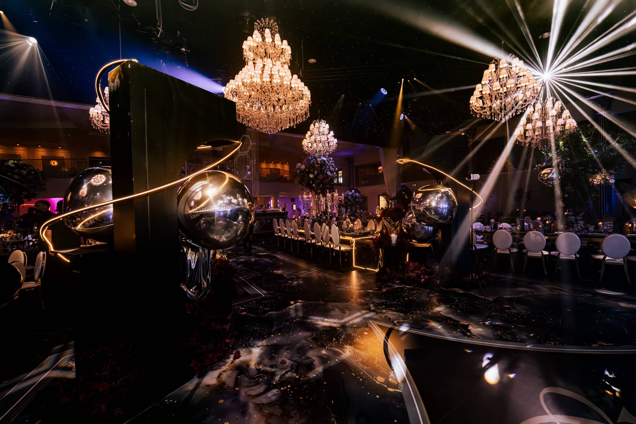Golden spheres and crystal chandeliers over seated guests in beam lighting, by Kudos AV