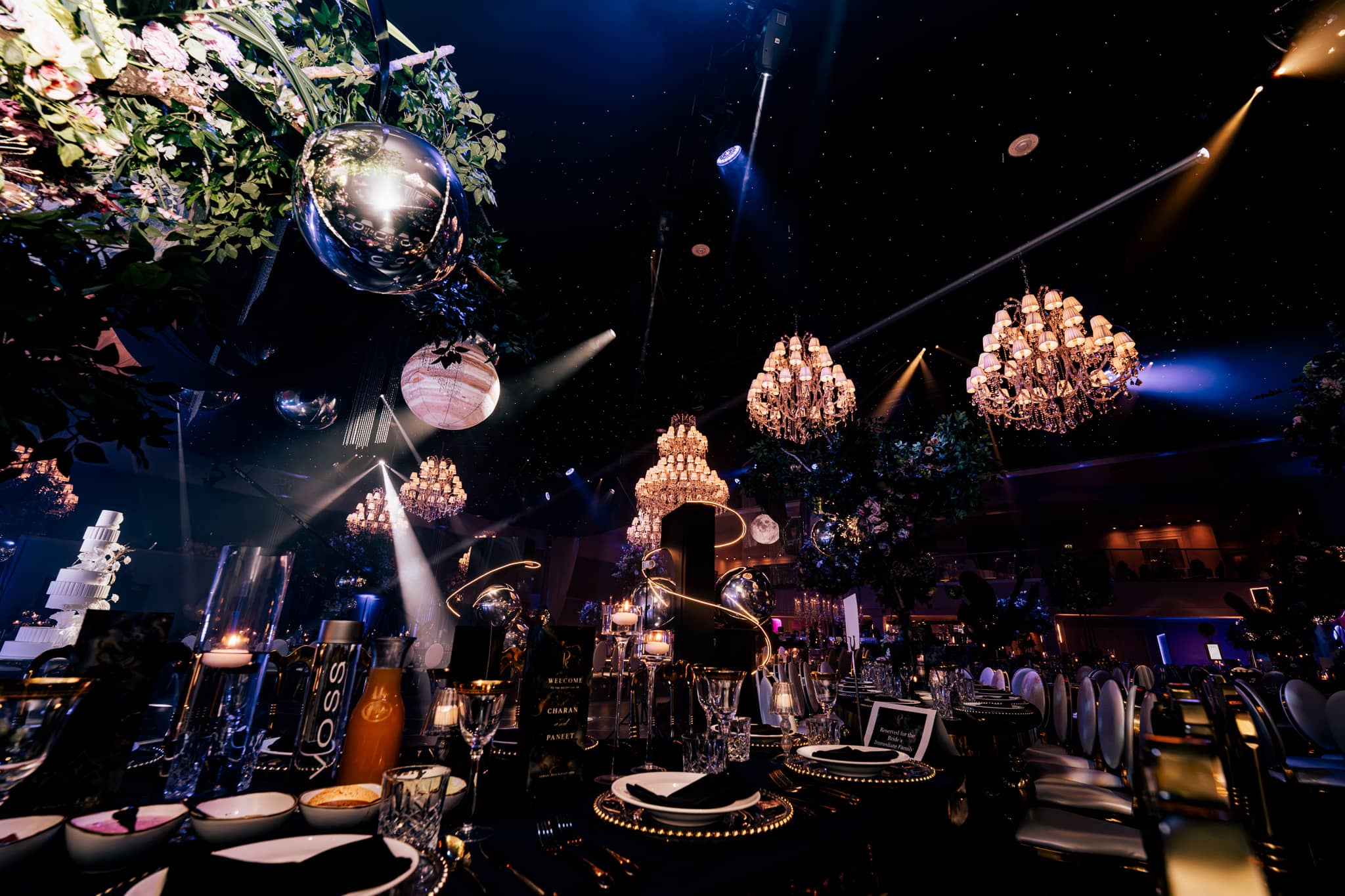 Gold accented table settings under chandeliers and uplighting, by Kudos AV