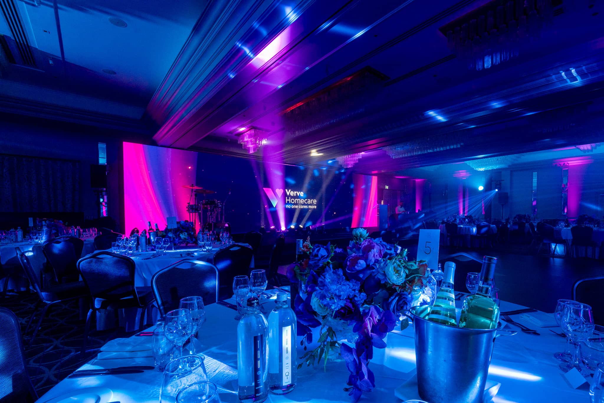 A Verve Awards Night table at Sopwell House with floral centrepiece, champagne and blue uplighting, looking towards the LED wall and stage.