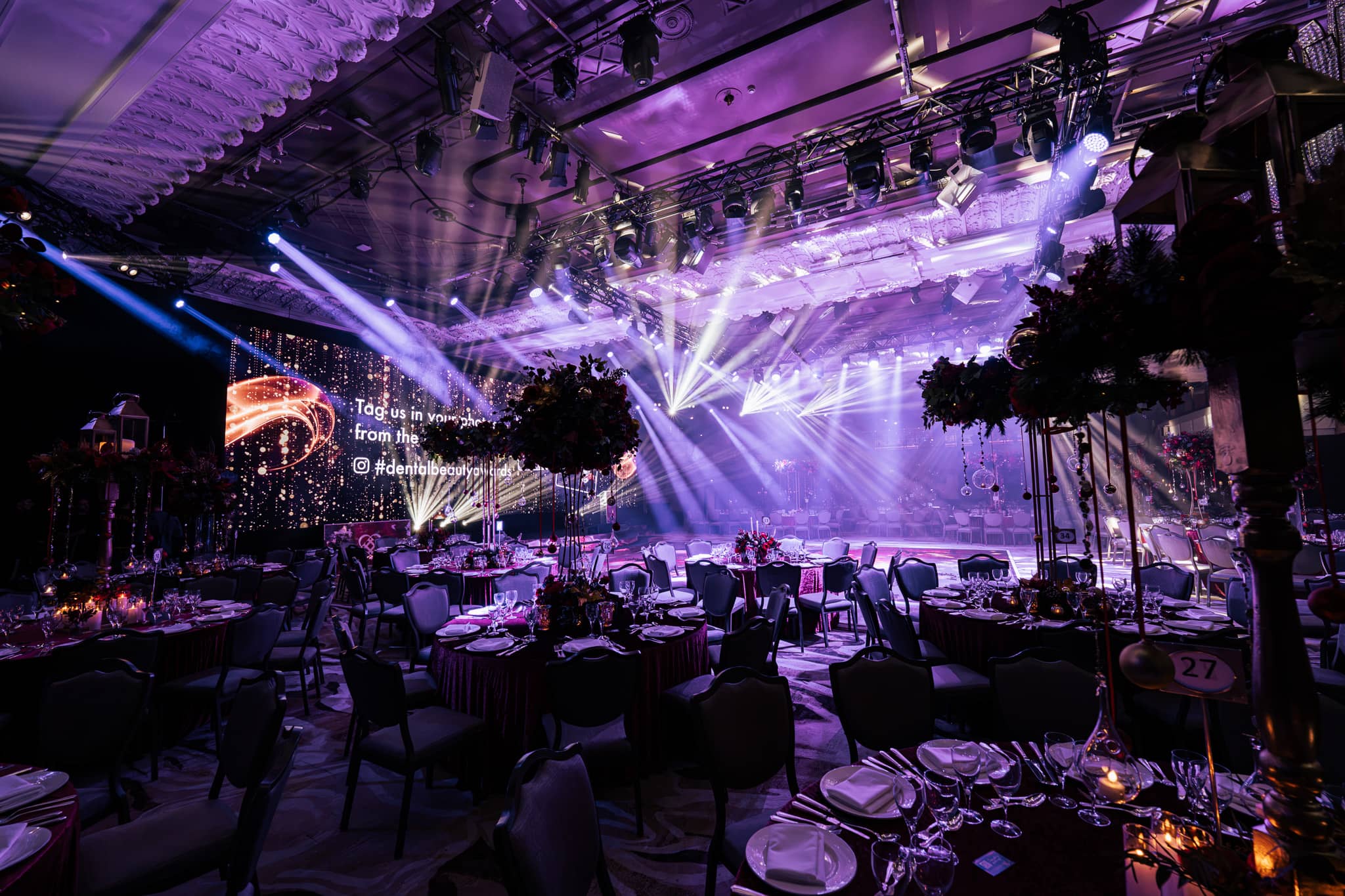 Purple uplighting around the Great Room and the lighting rig over the stage, tables dressed for the Dental Beauty Partners Awards 2025 dinner at Grosvenor House London, by Kudos AV.