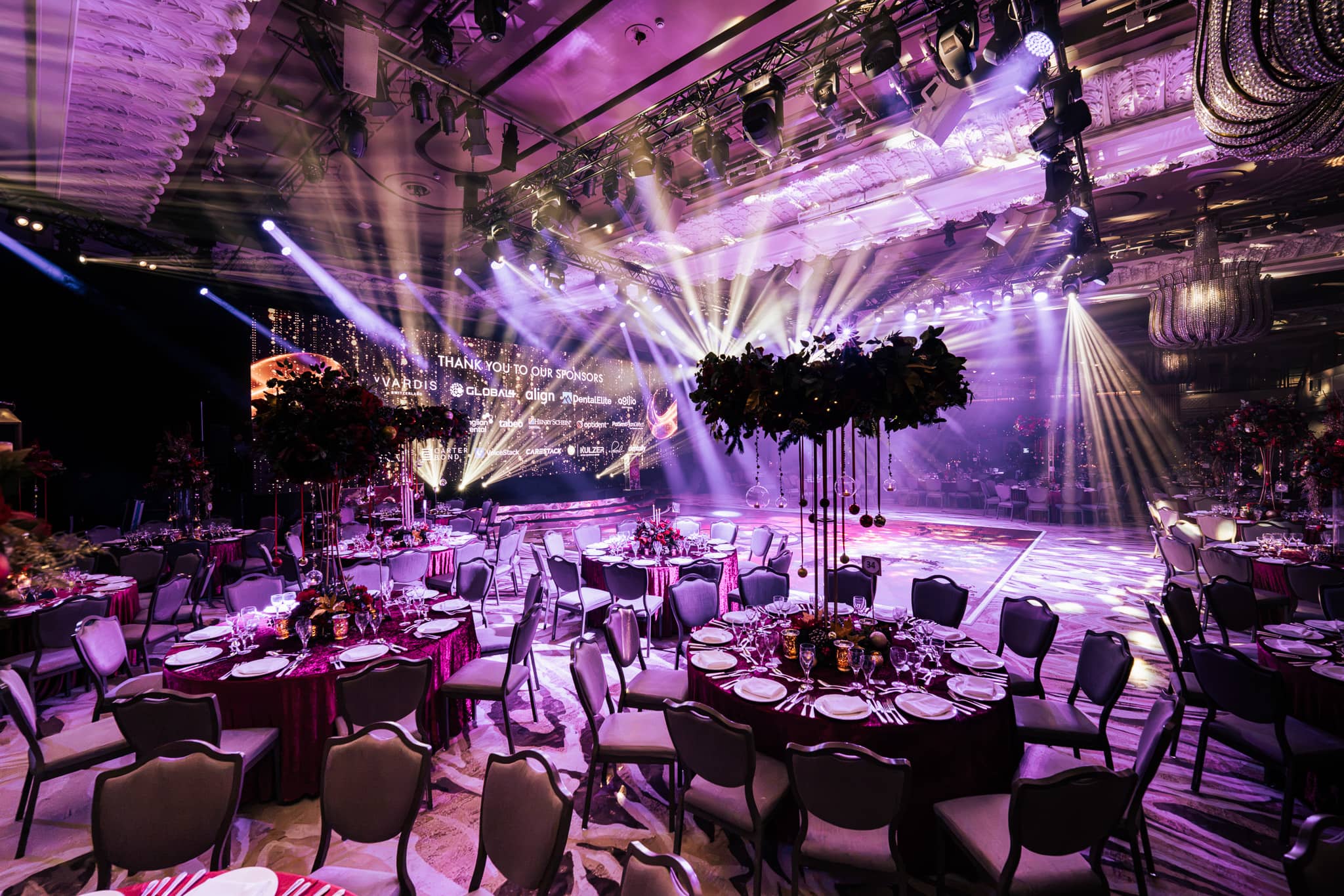 Purple uplighting and suspended floral installations, the stage screen glowing at the far end of the Great Room at Grosvenor House London, Dental Beauty Partners Awards 2025 by Kudos AV.
