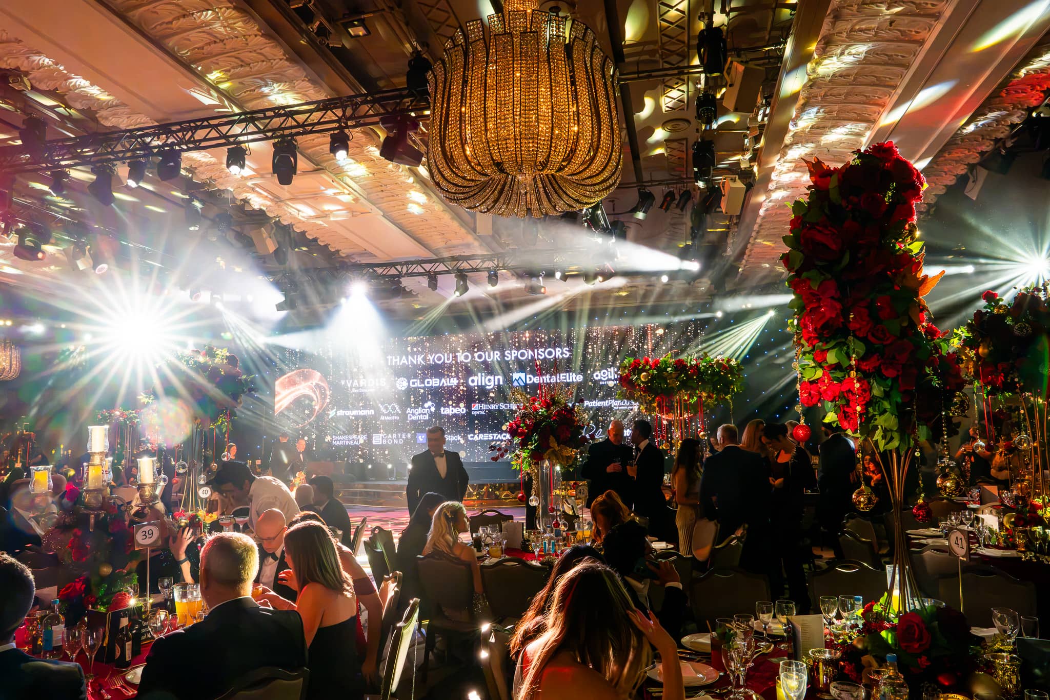 Red floral installations and the partner backdrop under stage lighting, Dental Beauty Partners Awards 2025 in the Great Room at Grosvenor House London, by Kudos AV.