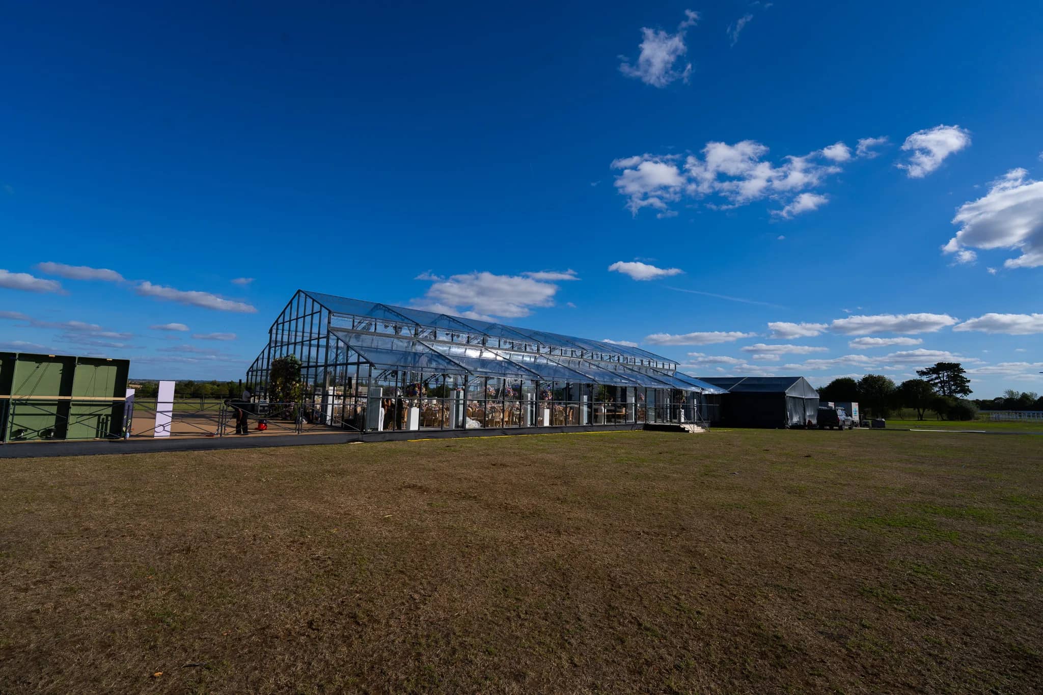 The glass marquee from the side with the catering tent joined to its end, on parkland in Warwickshire, by Kudos AV