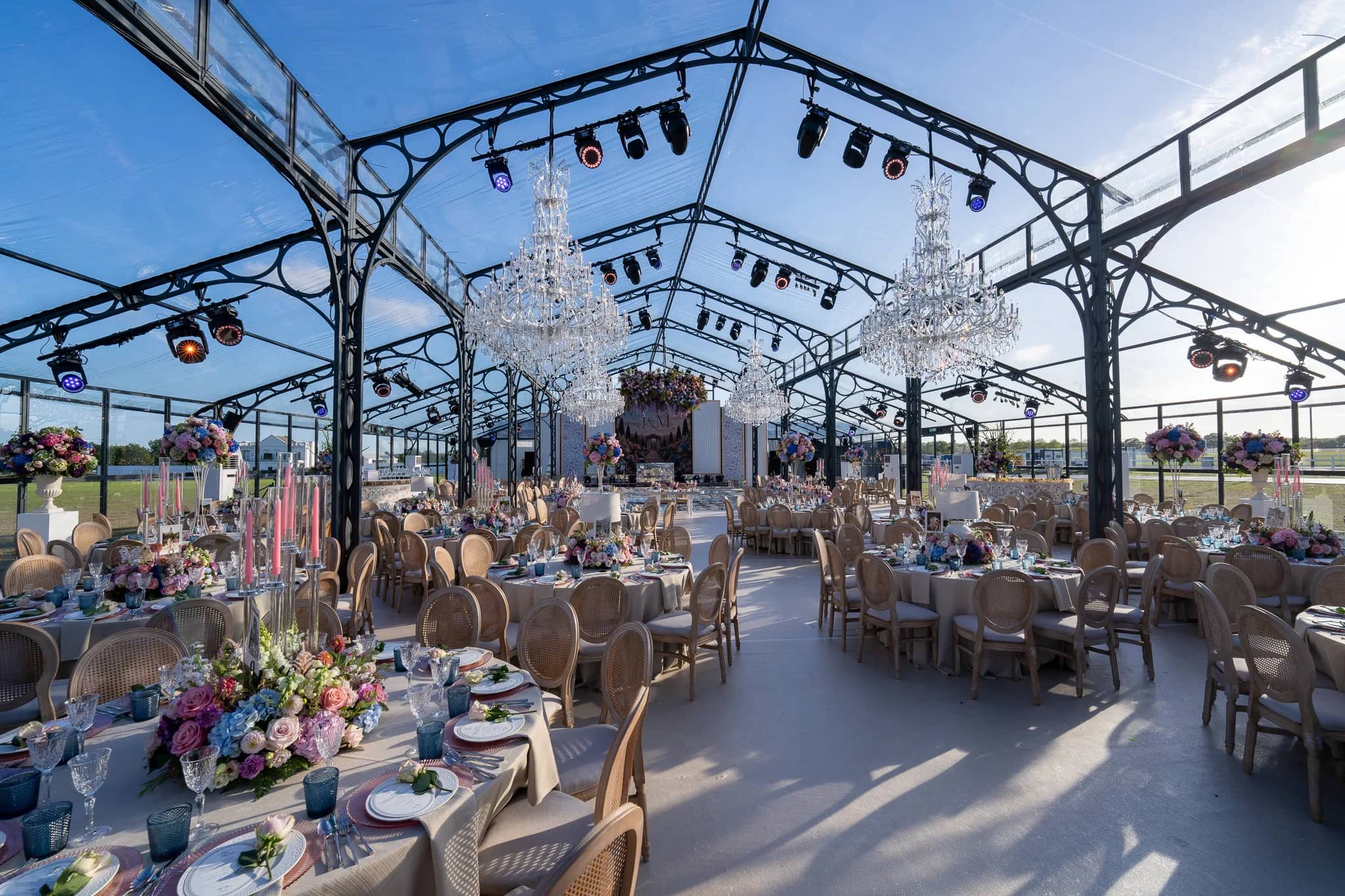 The tables set and the chandeliers hung, looking down a glass marquee to the stage and the florals over the dancefloor before the guests arrived, Warwickshire, by Kudos AV