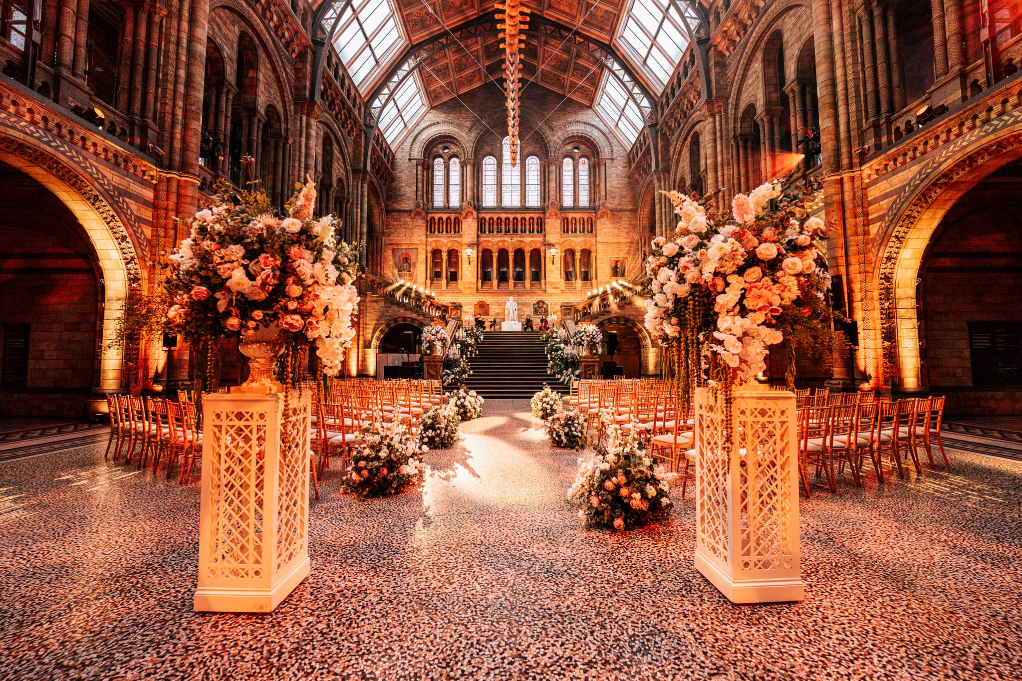 Floral installations and uplighting on the Hintze Hall stonework for a wedding ceremony at the Natural History Museum, by Kudos AV.
