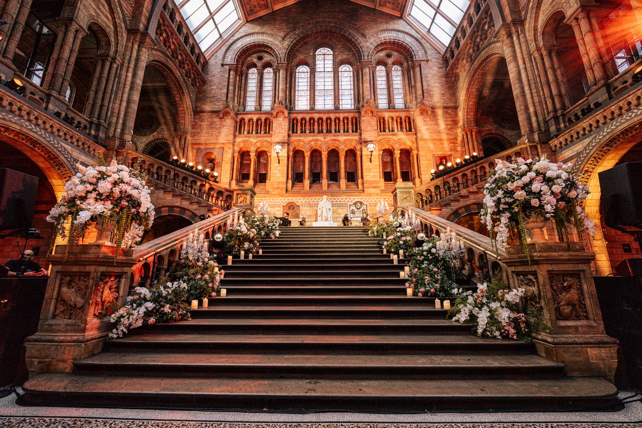 White florals and uplighting on the Hintze Hall staircase, the backdrop for the wedding ceremony at the Natural History Museum, by Kudos AV.