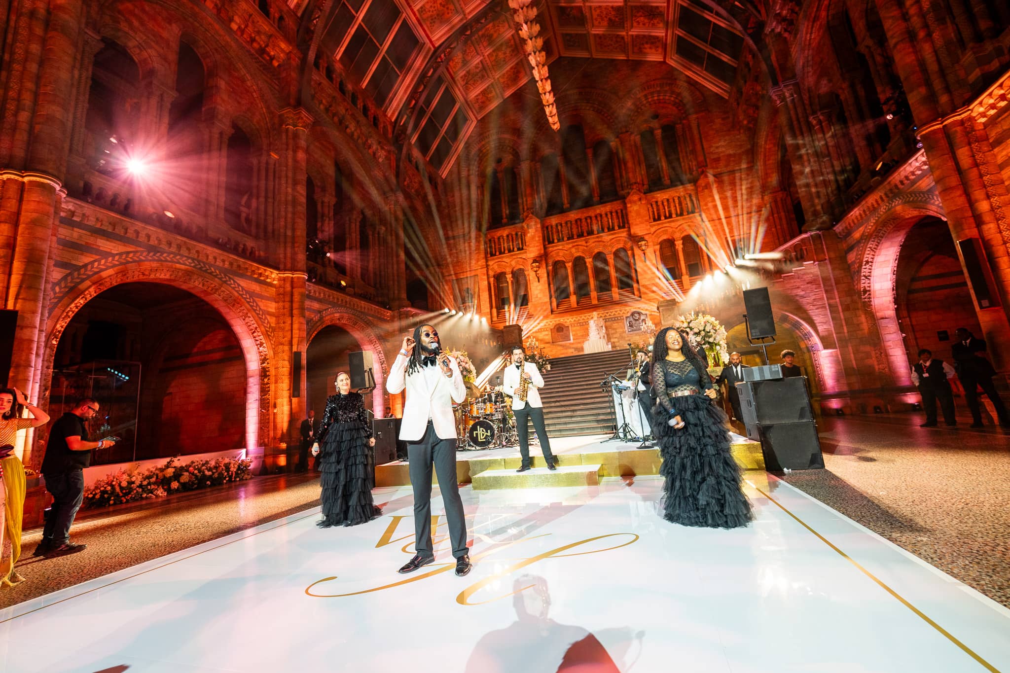 A performance at the front of Hintze Hall under red lighting, the ornate arches lit behind, at a Natural History Museum wedding by Kudos AV.