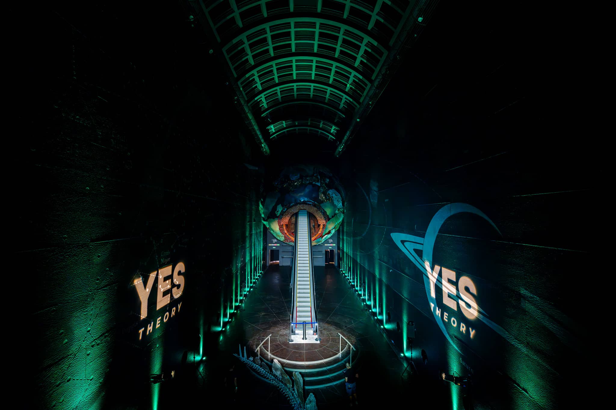Earth Hall lit green for the Yes Theory 10 million subscriber celebration, the Yes Theory name projected on the walls either side of the escalator, by Kudos AV.