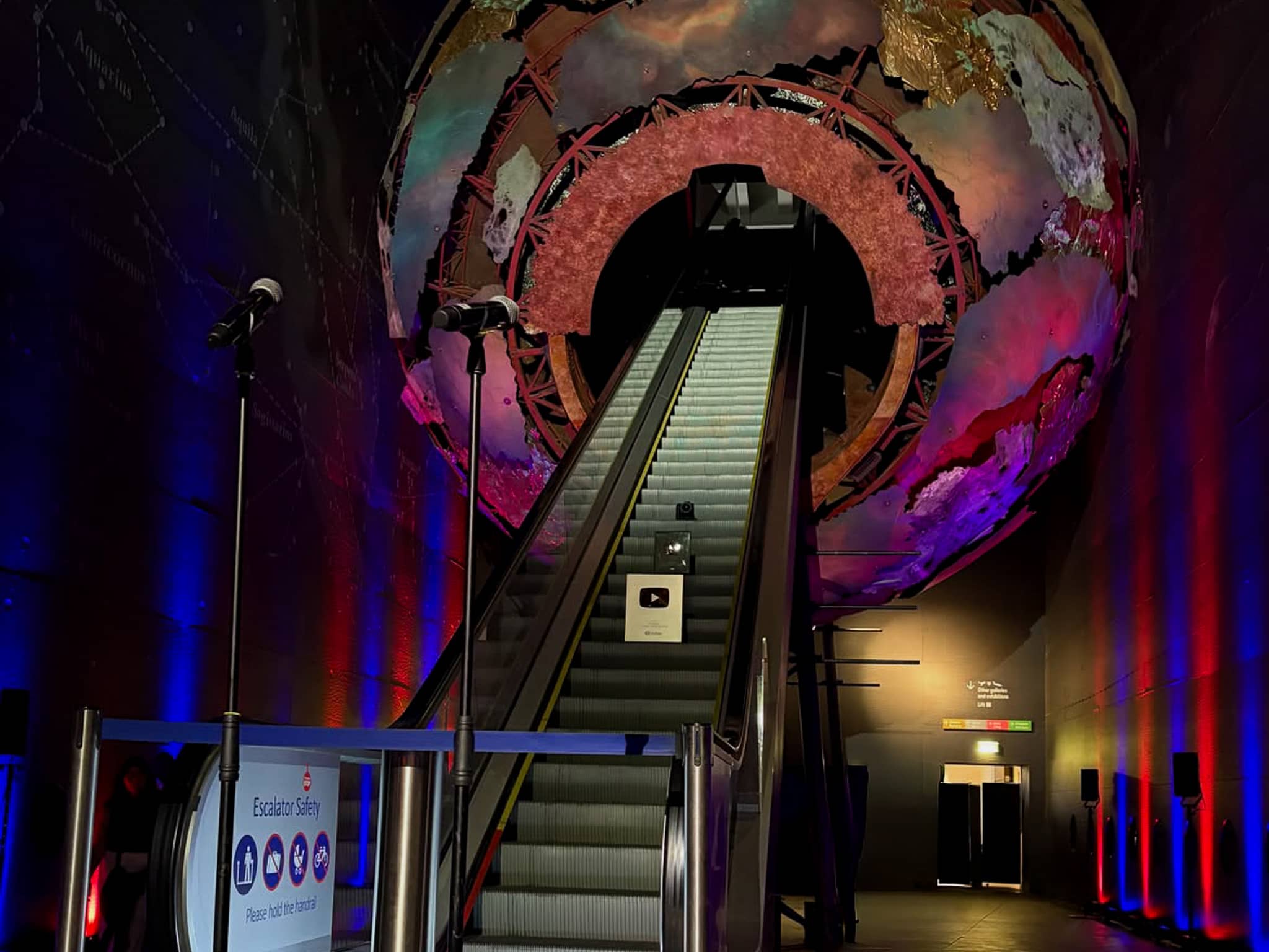 The escalator and Earth sculpture in Earth Hall under purple and blue lighting at the Yes Theory 10 million subscriber celebration, by Kudos AV.