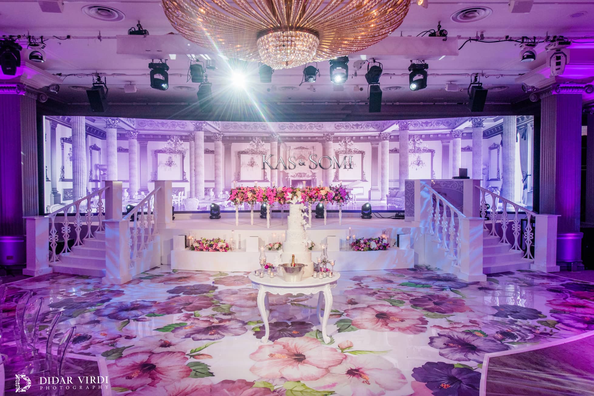 Two white staircases with decorative balustrades frame curved stage tiers beneath the LED screen at the Grosvenor House Ballroom wedding.