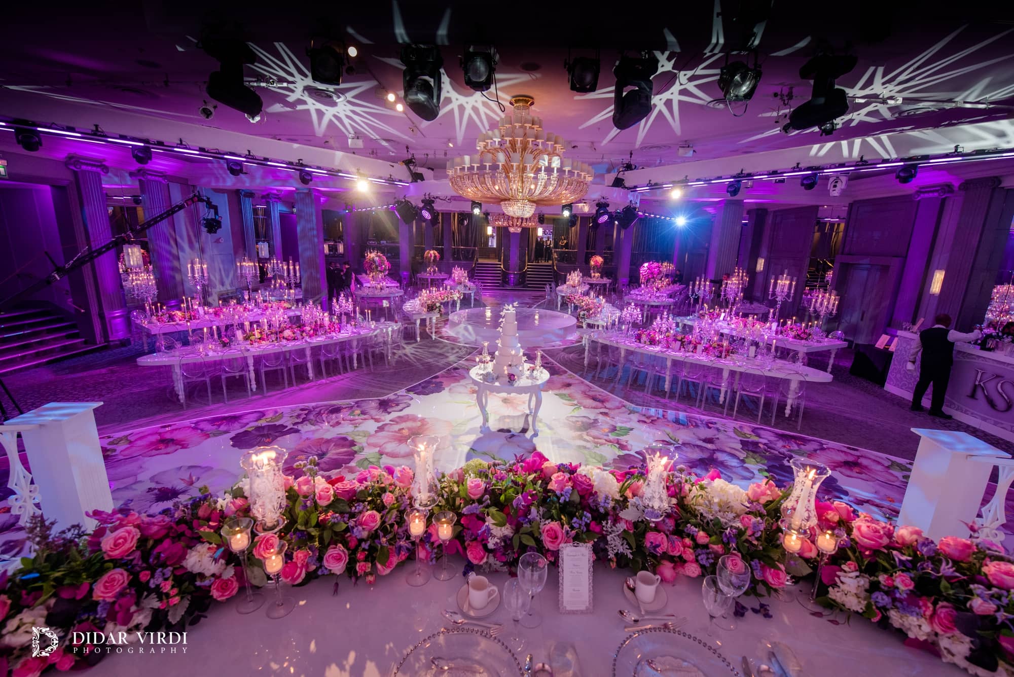 Overhead moving lights cast patterned gobos across the Grosvenor House Ballroom ceiling above the wedding tables and floral walkway.