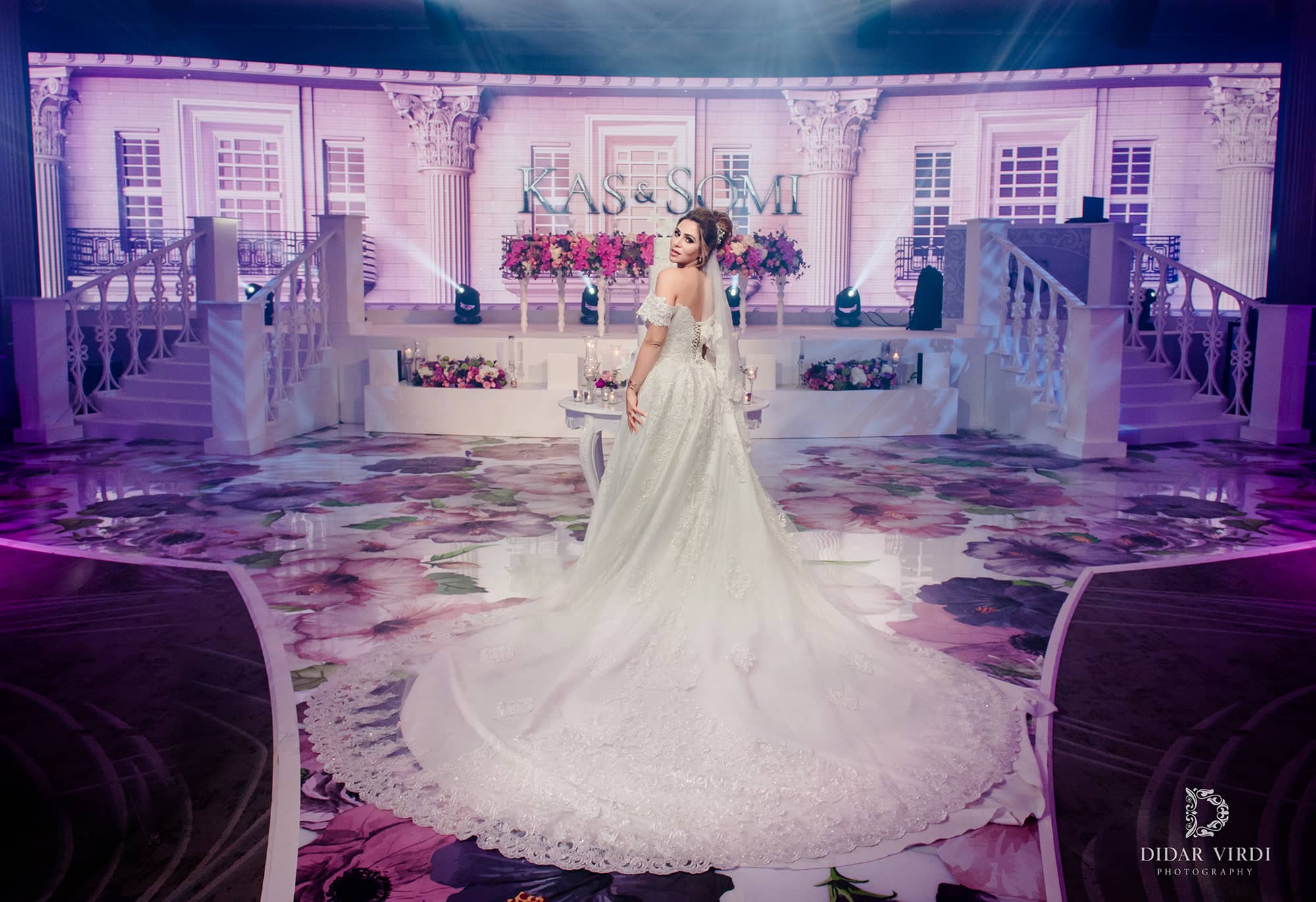 A bride stands on the floral walkway before the white staircase set and architectural LED backdrop at Grosvenor House London.