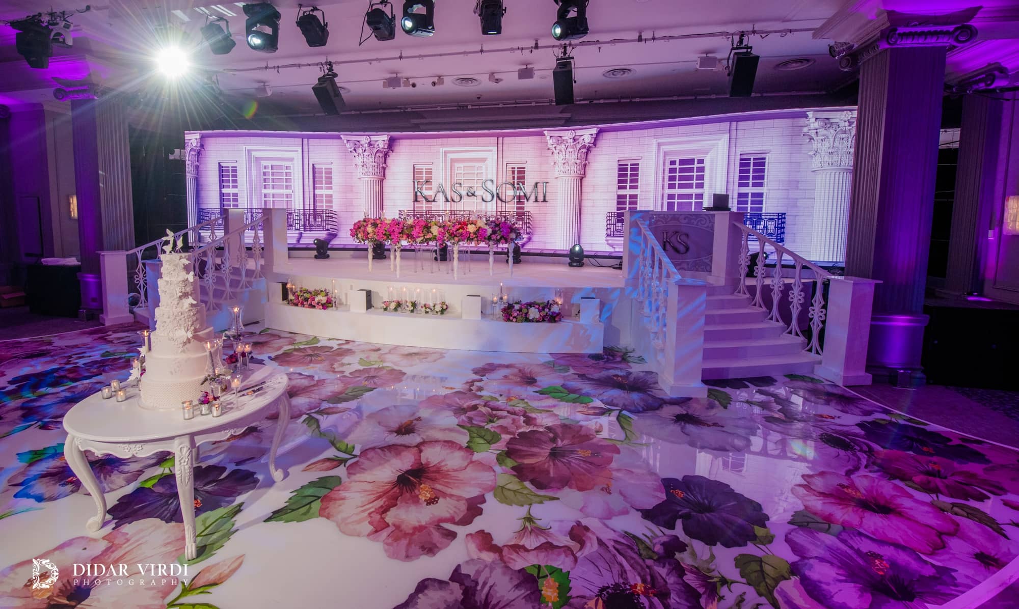 Floral floor graphics lead past a cake display to white stage steps and a curved LED backdrop in the Grosvenor House Ballroom.