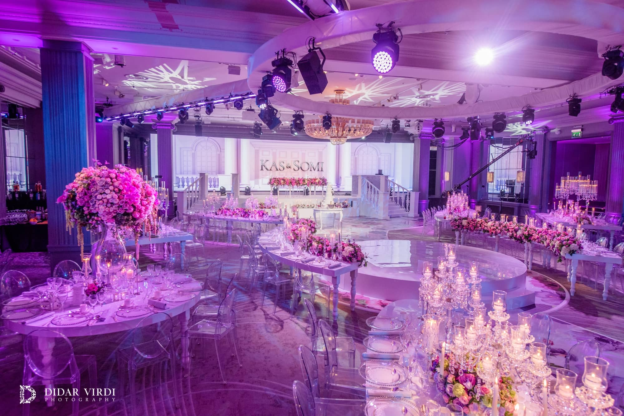 Oval and curved guest tables beside a floral walkway, facing the white staircase set and LED screen at Grosvenor House.