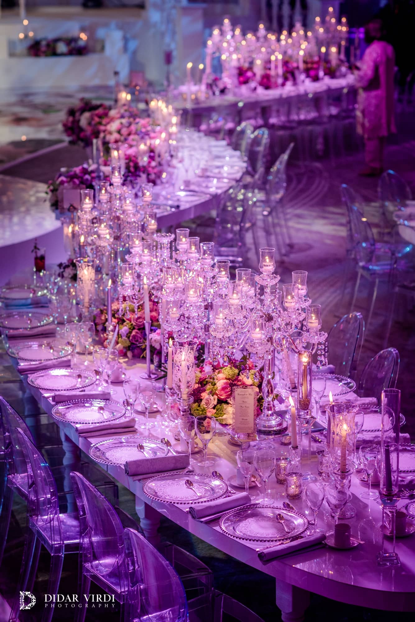 A curved dining table set with candles, glassware and flowers under purple lighting in the Grosvenor House Ballroom.